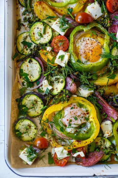 These Baked Eggs are so fun and easy to make! Eggs are baked in the oven on a sheet pan cradled inside rings of bell pepper along with roasted potatoes, zucchini, and tomatoes. Top them with feta and fresh herbs.