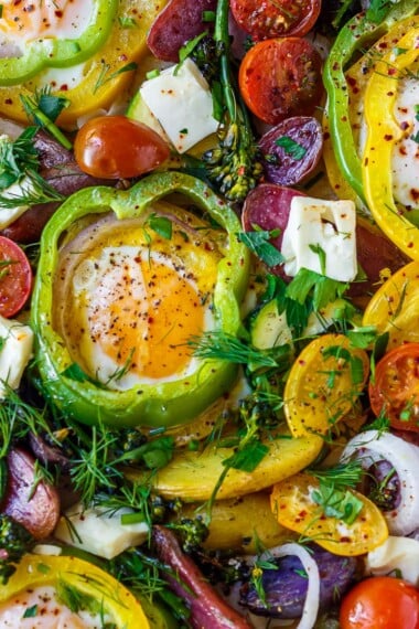 These Baked Eggs are so fun and easy to make! Eggs are baked in the oven on a sheet pan cradled inside rings of bell pepper along with roasted potatoes, zucchini, and tomatoes. Top them with feta and fresh herbs.