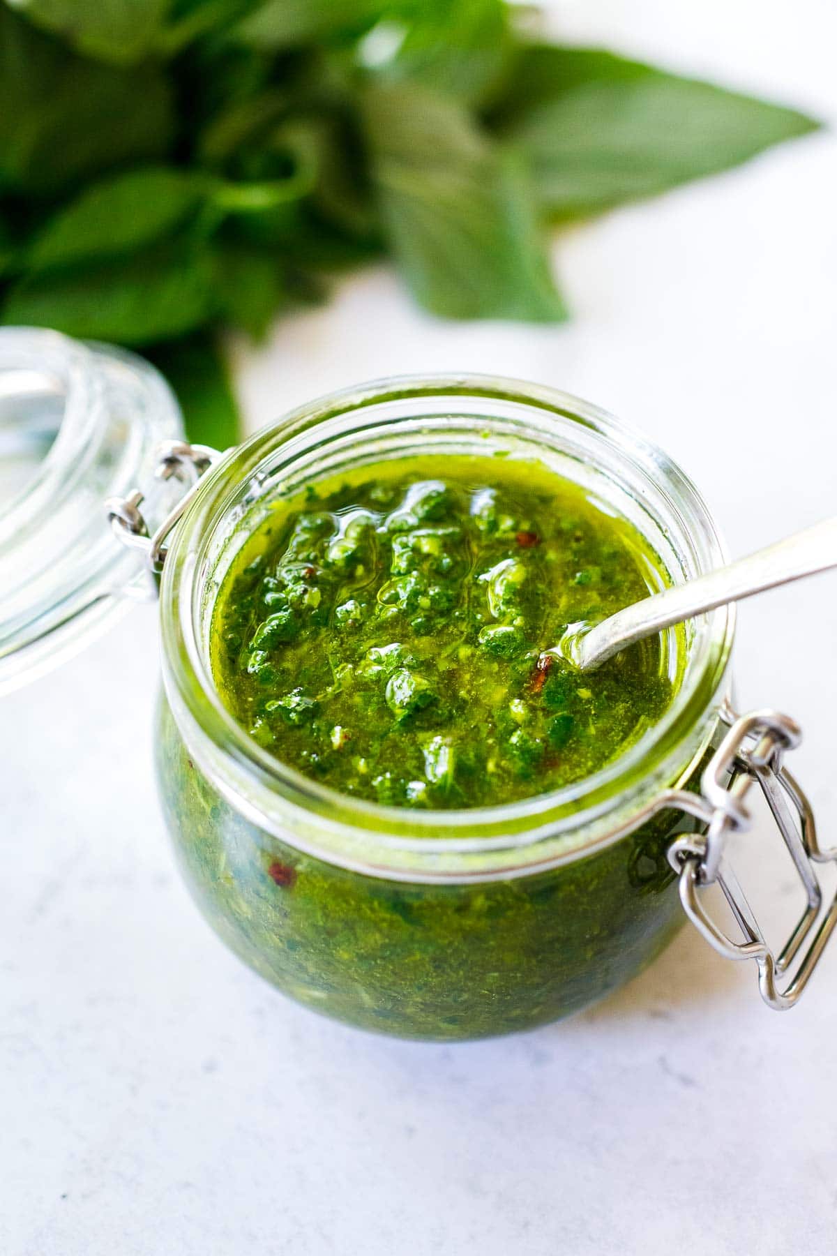 A jar of Basil Oil with a spoon. Made with fresh basil, garlic, olive oil, lemon, salt, and pepper,  in just a few minutes. 