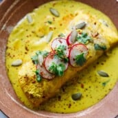 shrimp enchiladas, one of our most popular Mexican recipes, in a yellow sauce garnished with pumpkin seeds, radishes, and cilantro.