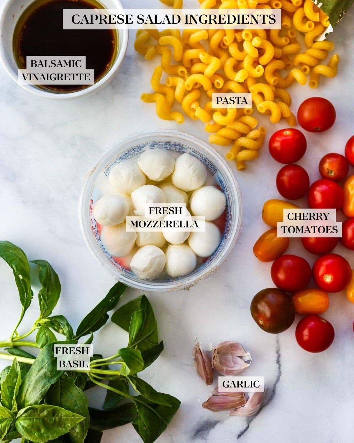 caprese pasta salad ingredients - balsamic and oil in a bowl, mozzarella balls, fresh basil, garlic cloves, cherry tomatoes, and cappellini pasta.