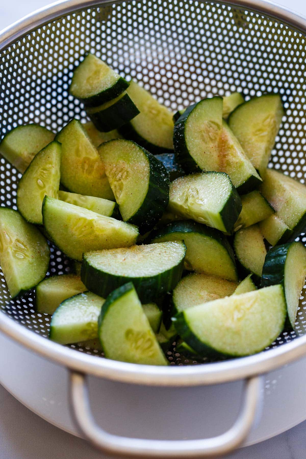Salted cucumbers in a colander for Korean Cucumber Salad.
