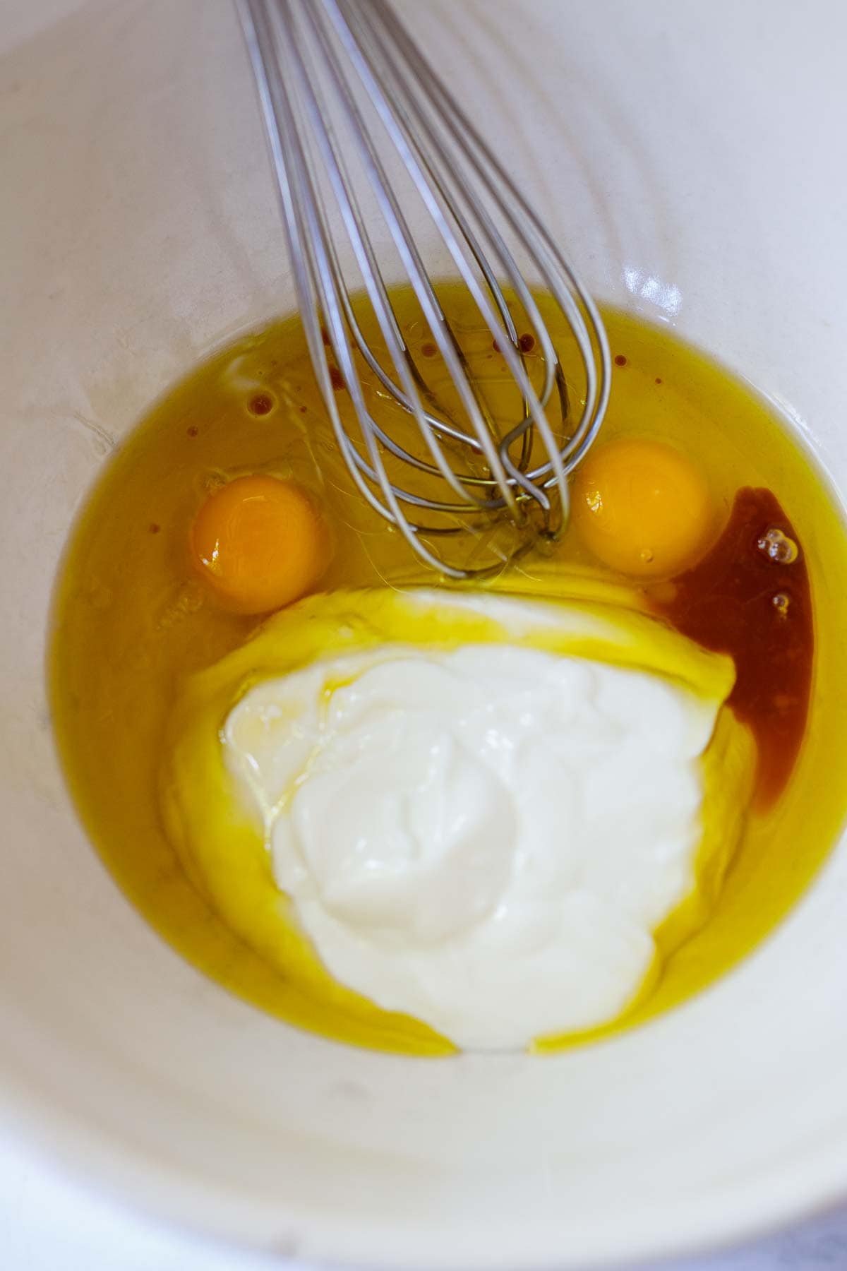 mixing the eggs, vanilla, yogurt and oil with a whisk in a white bowl. 