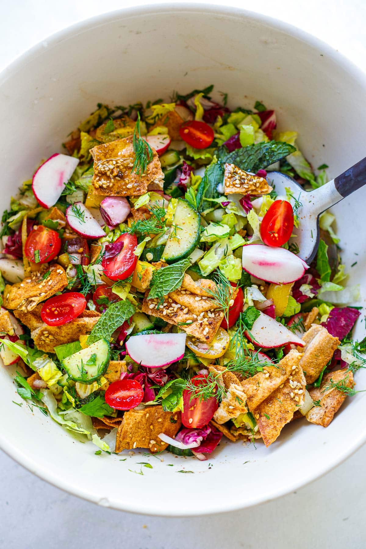 Tossing the Fattoush salad with the pita chips and lettuce in a large white bowl. 