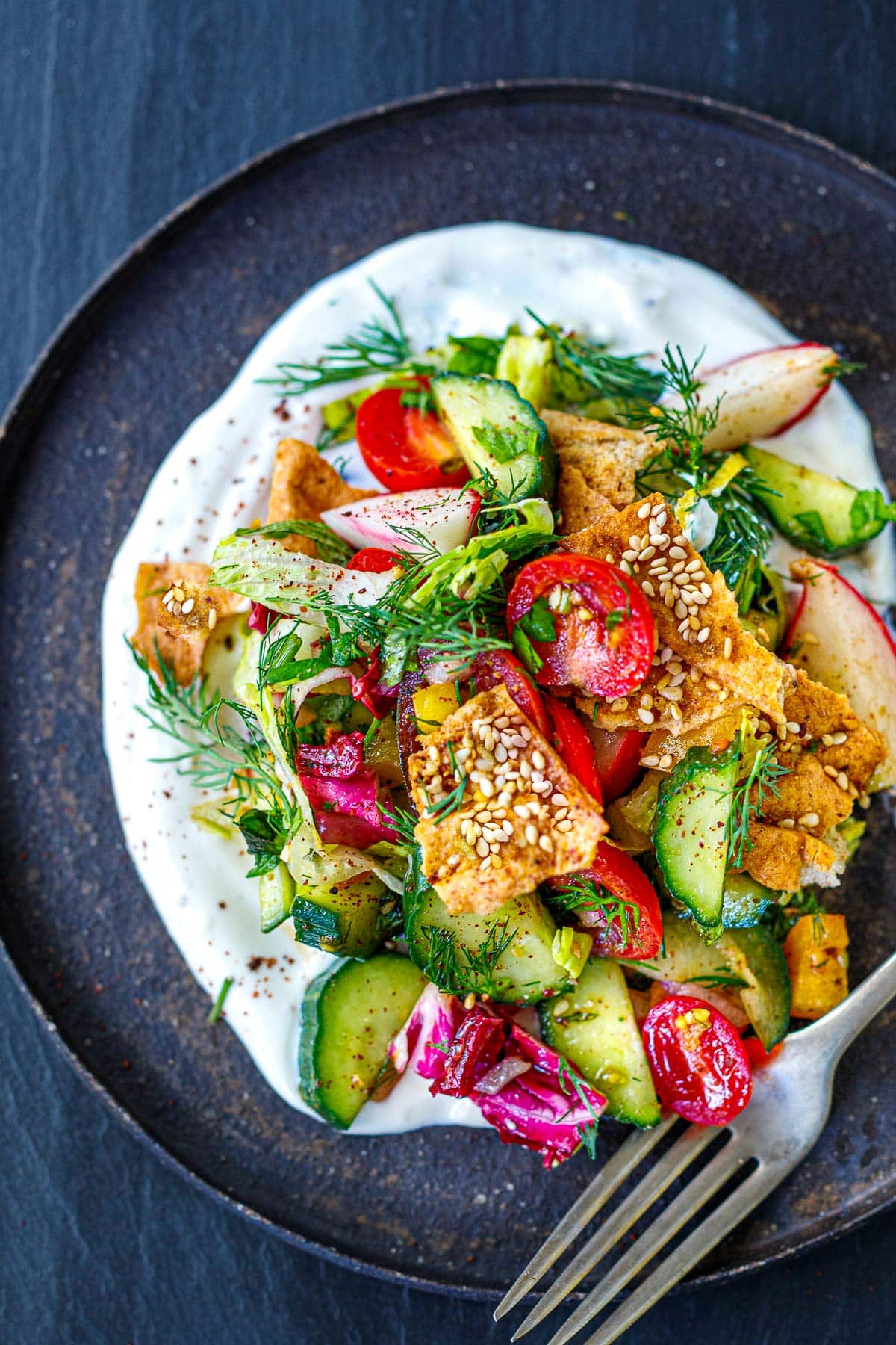This Fattoush recipe is fresh, light and flavorful, made with chopped vegetables, fresh herbs and toasty pita chips in a tangy sumac dressing, all piled over a creamy yogurt-tahini sauce.