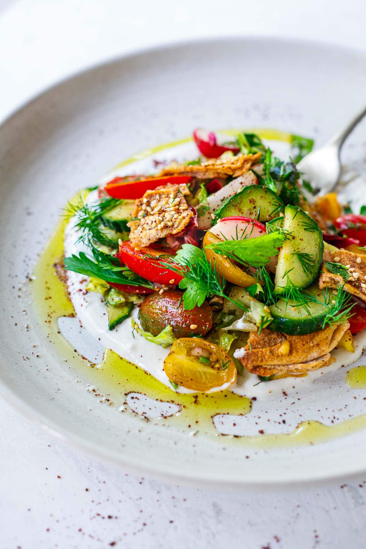 Fattoush Salad over creamy yogurt sauce with a drizzle of olive oil and sumac on a white plate. 