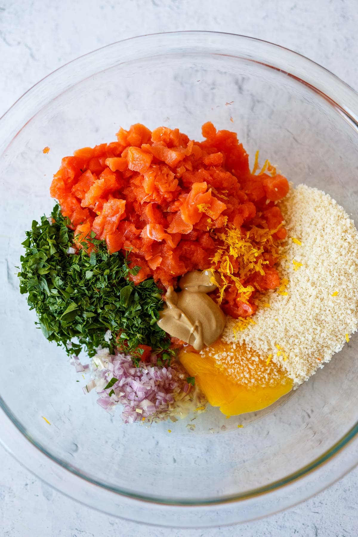 Salmon ingredients: chopped salmon, bread crumbs, parsley, dill, shallots, dijon and egg in a bowl.