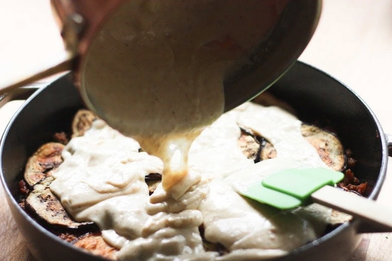 pouring béchamel sauce over eggplant slices to make moussaka.