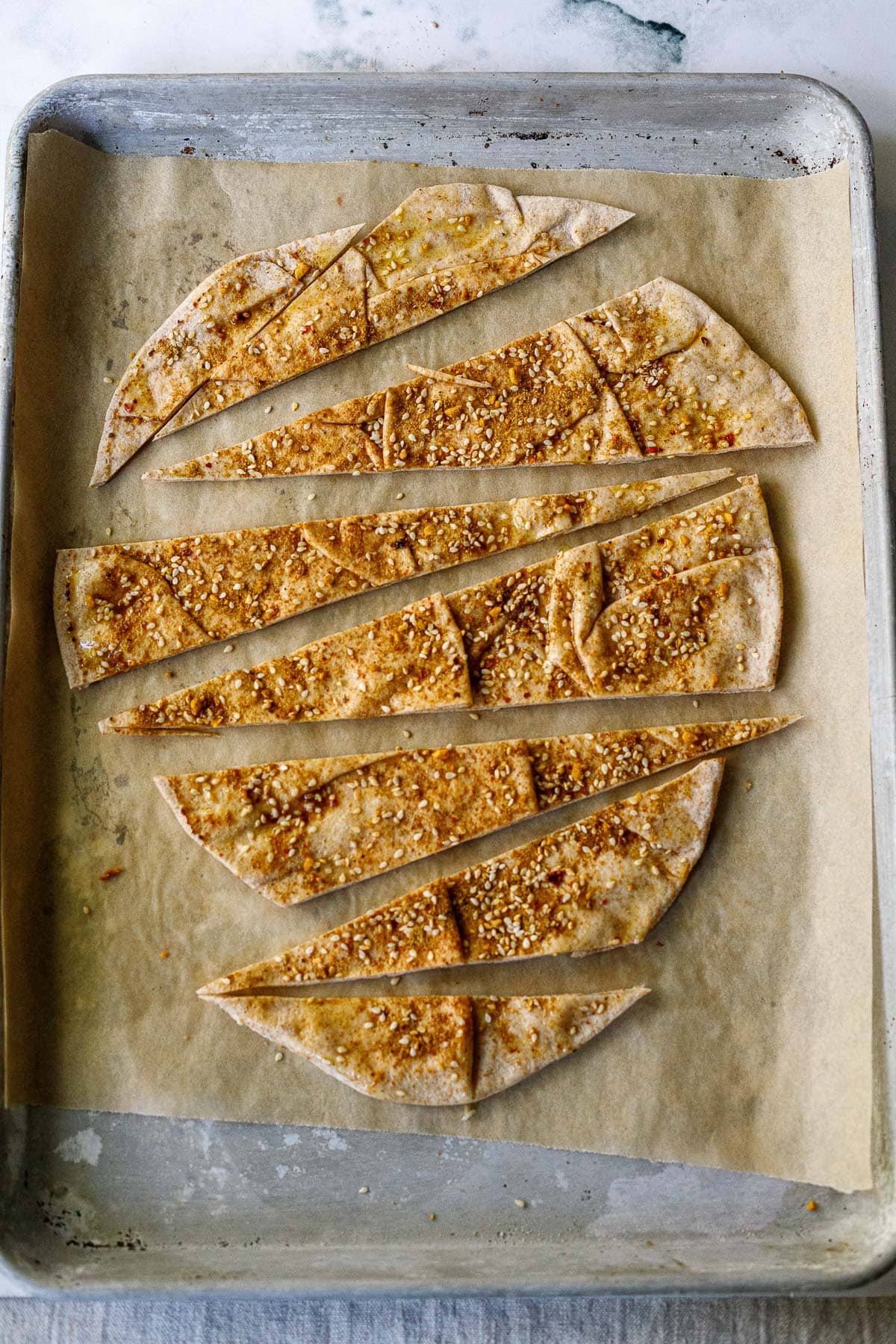 slices of pita bread with seasoning and sesame seeds on baking sheet