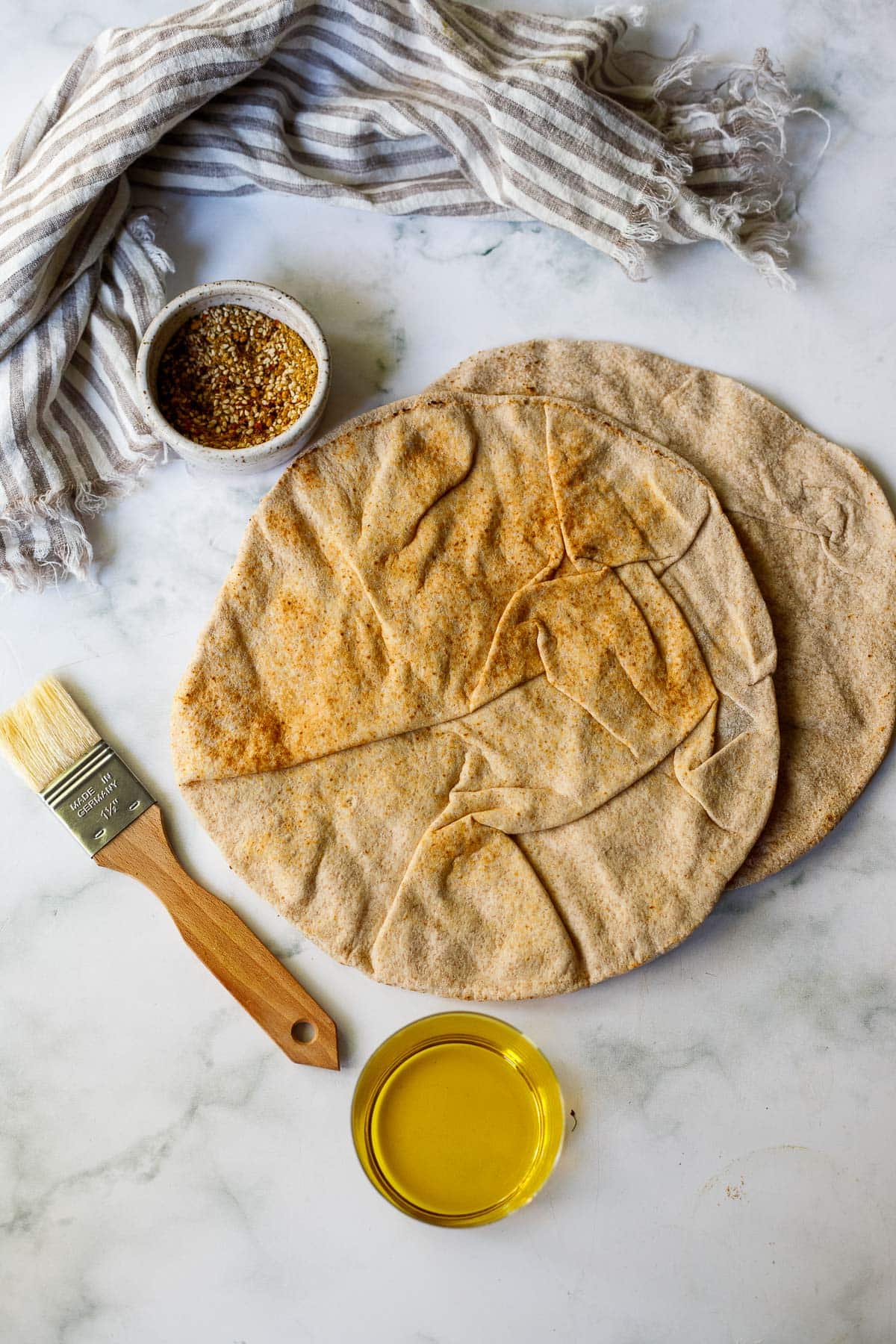 pita bread, olive oil, brush, and bowl of spices to make homemade pita chips