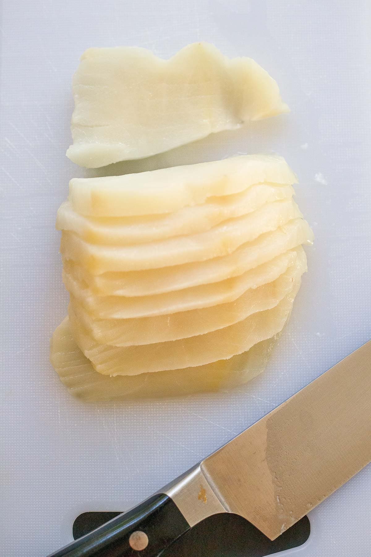 thin slices of raw fish on cutting board with knife.