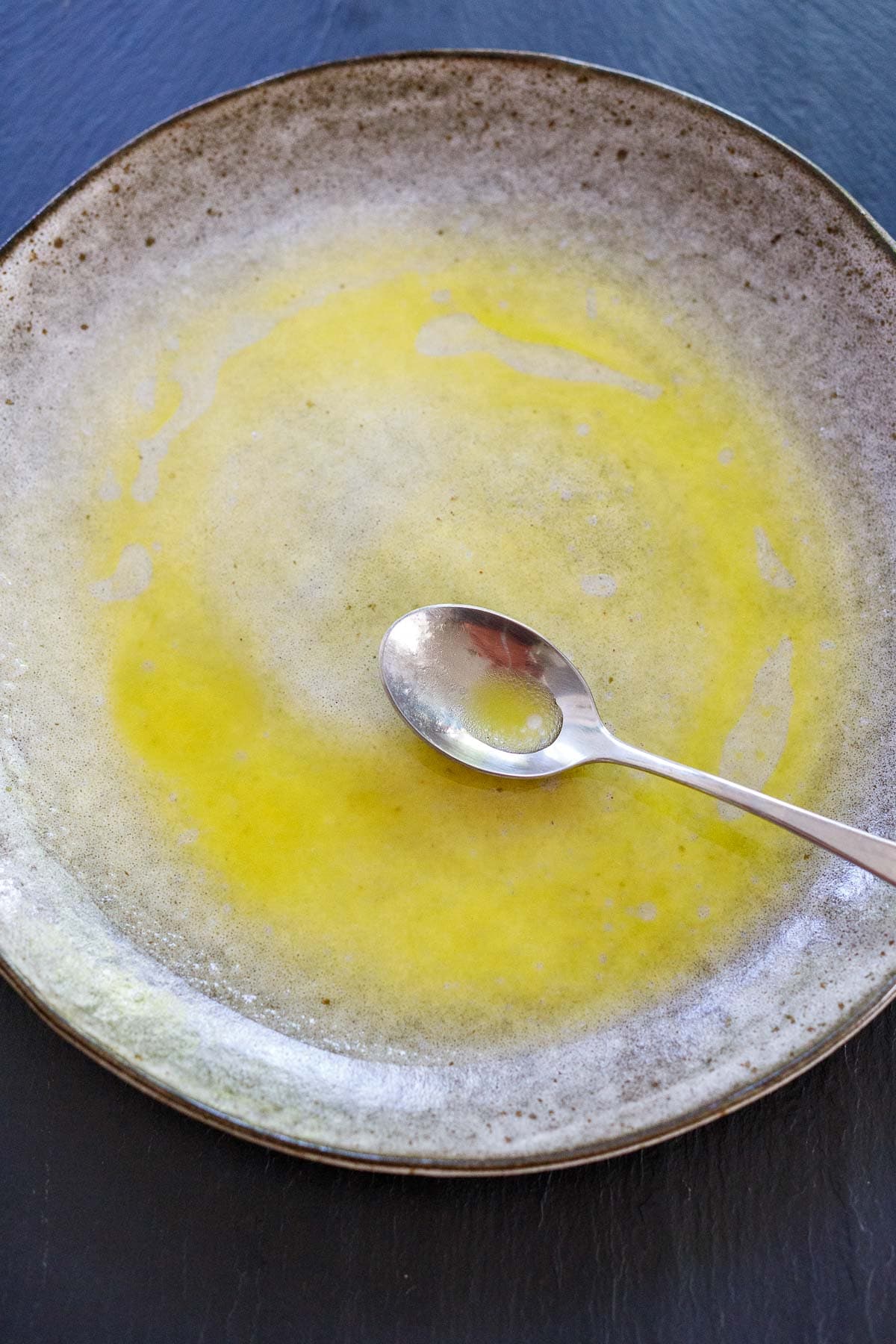 spoon spreading olive oil citrus dressing onto ceramic plate.
