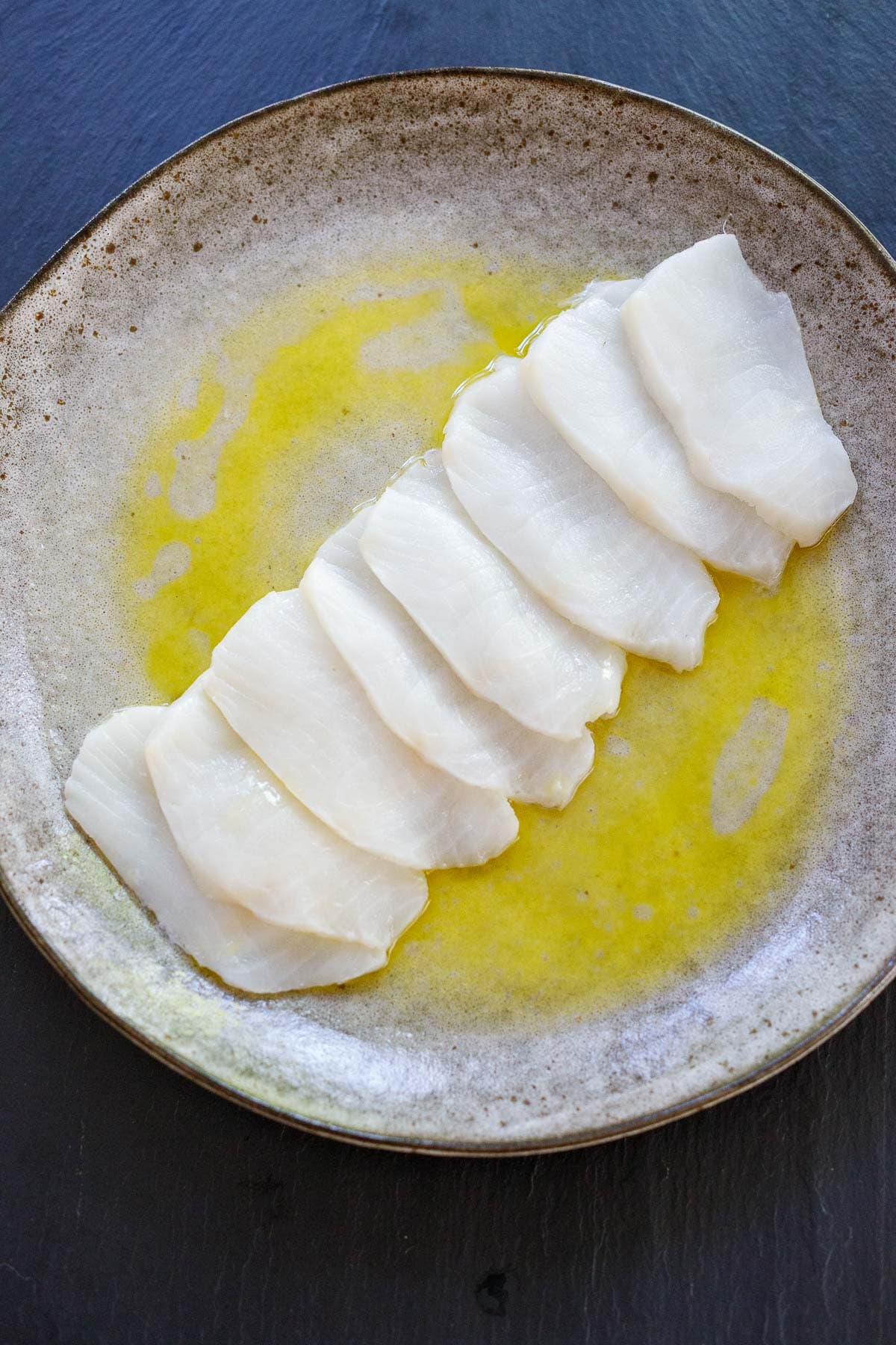 thin slices of raw fish arranged in a row on plate with olive oil