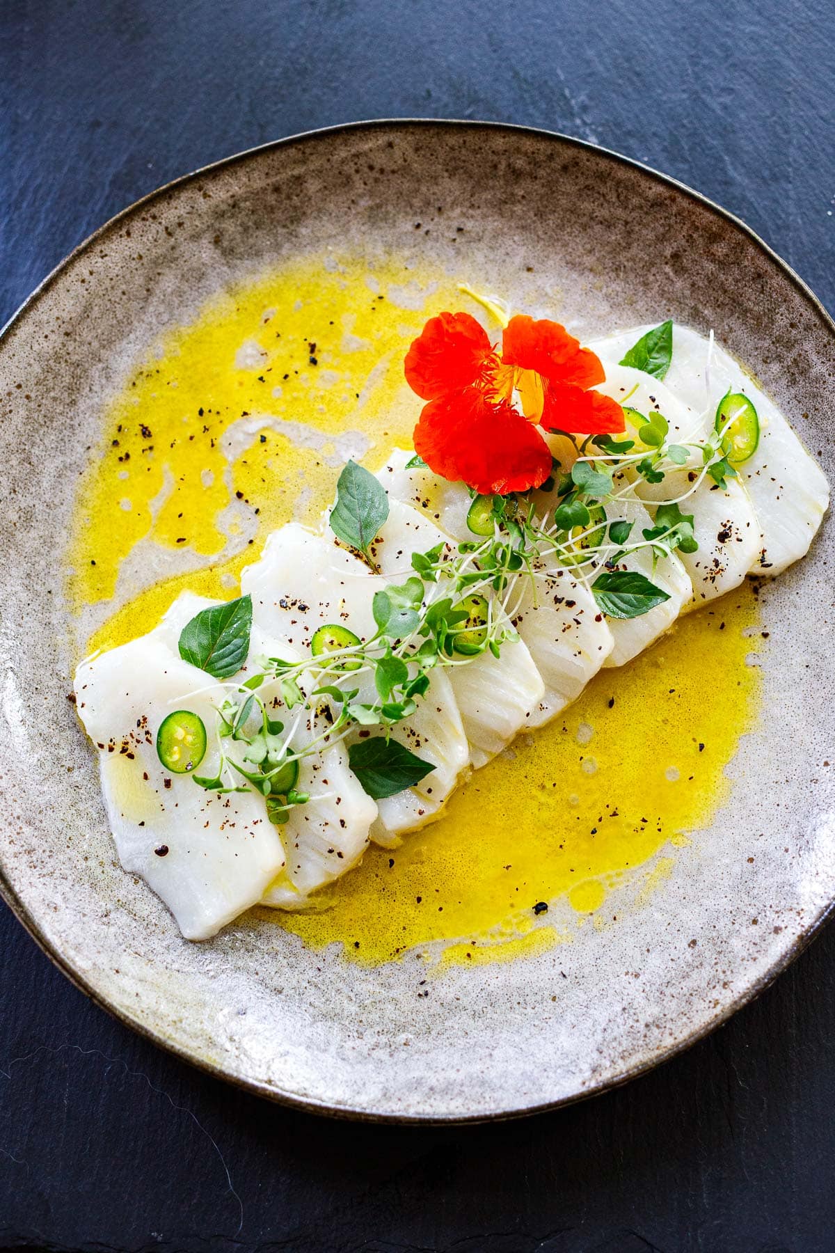 fresh fish crudo on plate with chilies, microgreens, and herbs