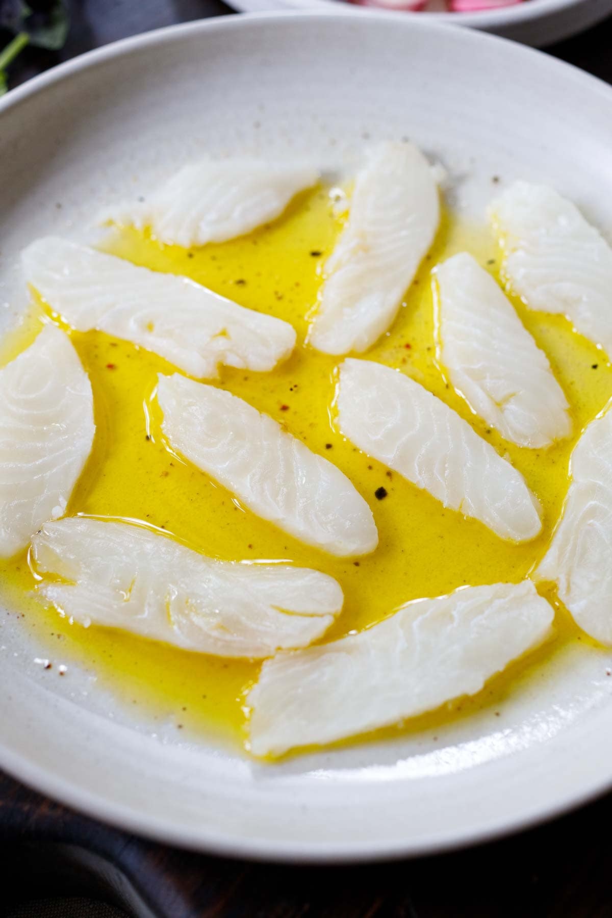 thin slices of raw fish arranged on plate with oil citrus dressing.