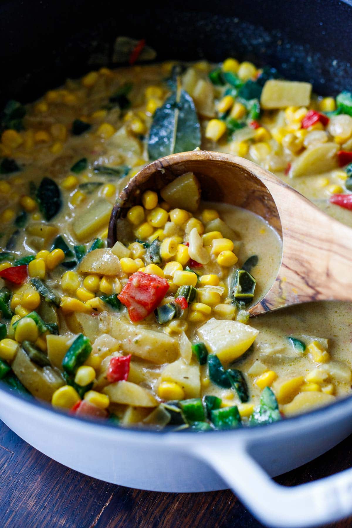 wood spoon stirring poblano corn chowder with peppers and potatoes