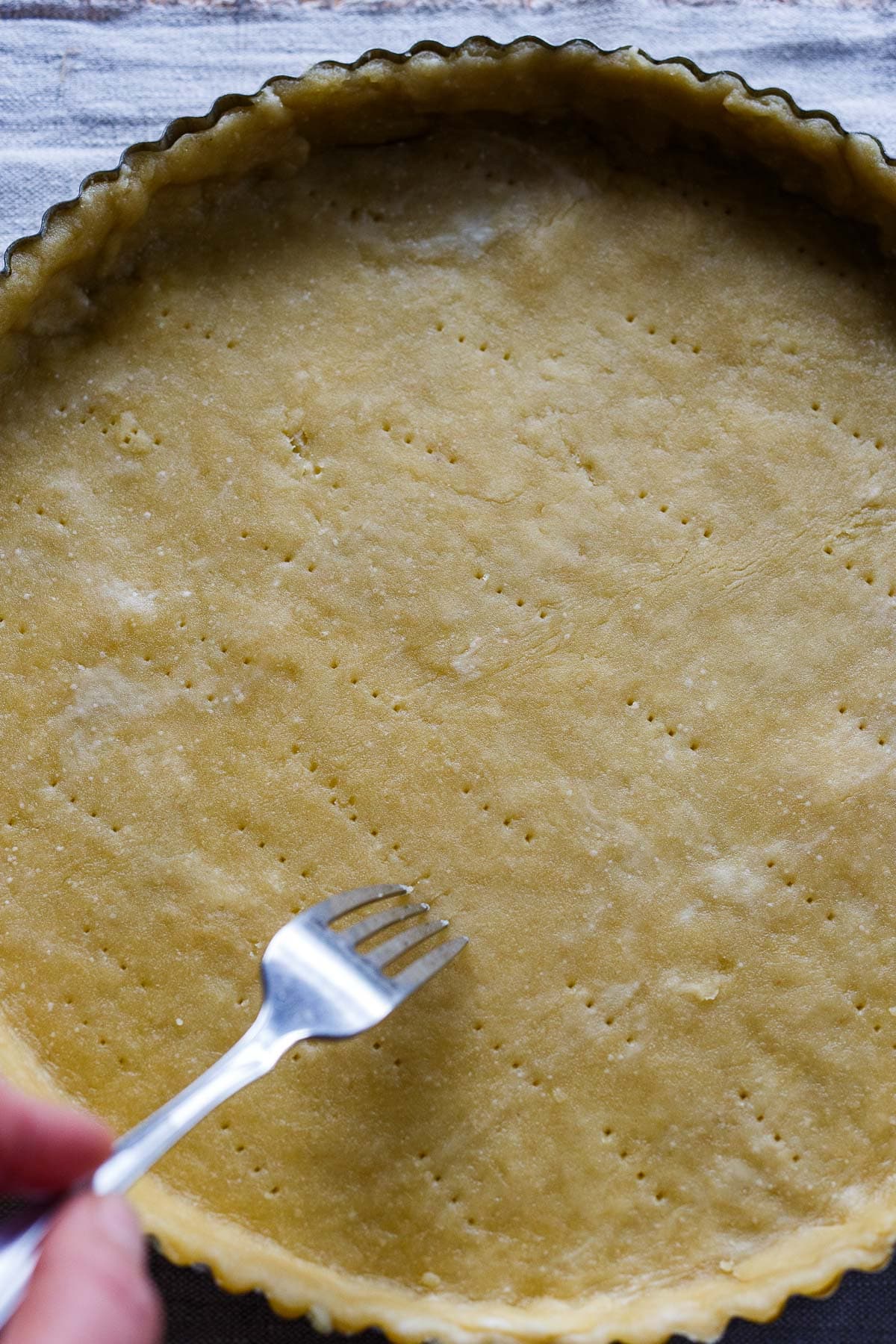 Dough in a tart pan with fork pokes for Tomato Tart.