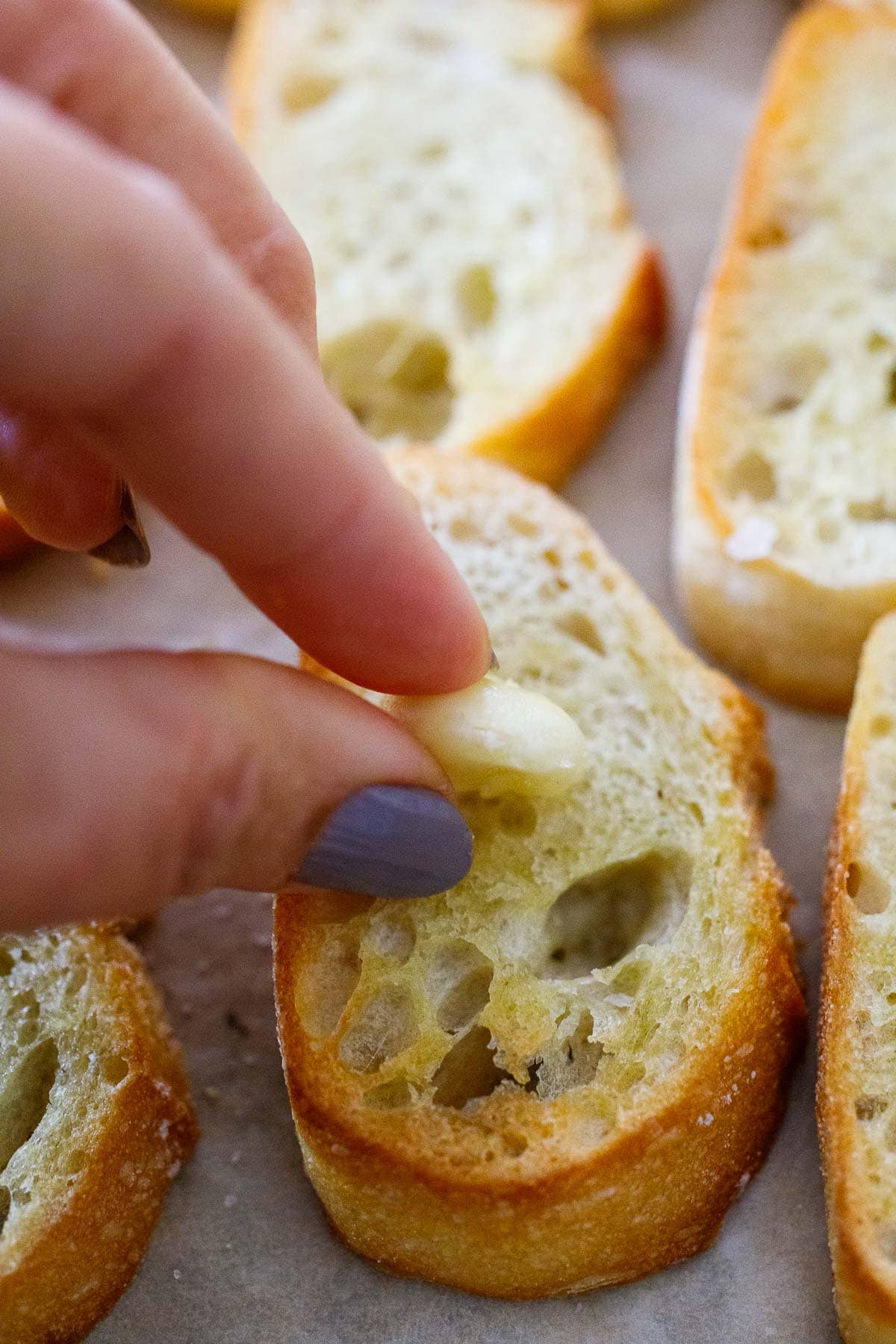 Two fingers rubbing raw garlic over baguette slice