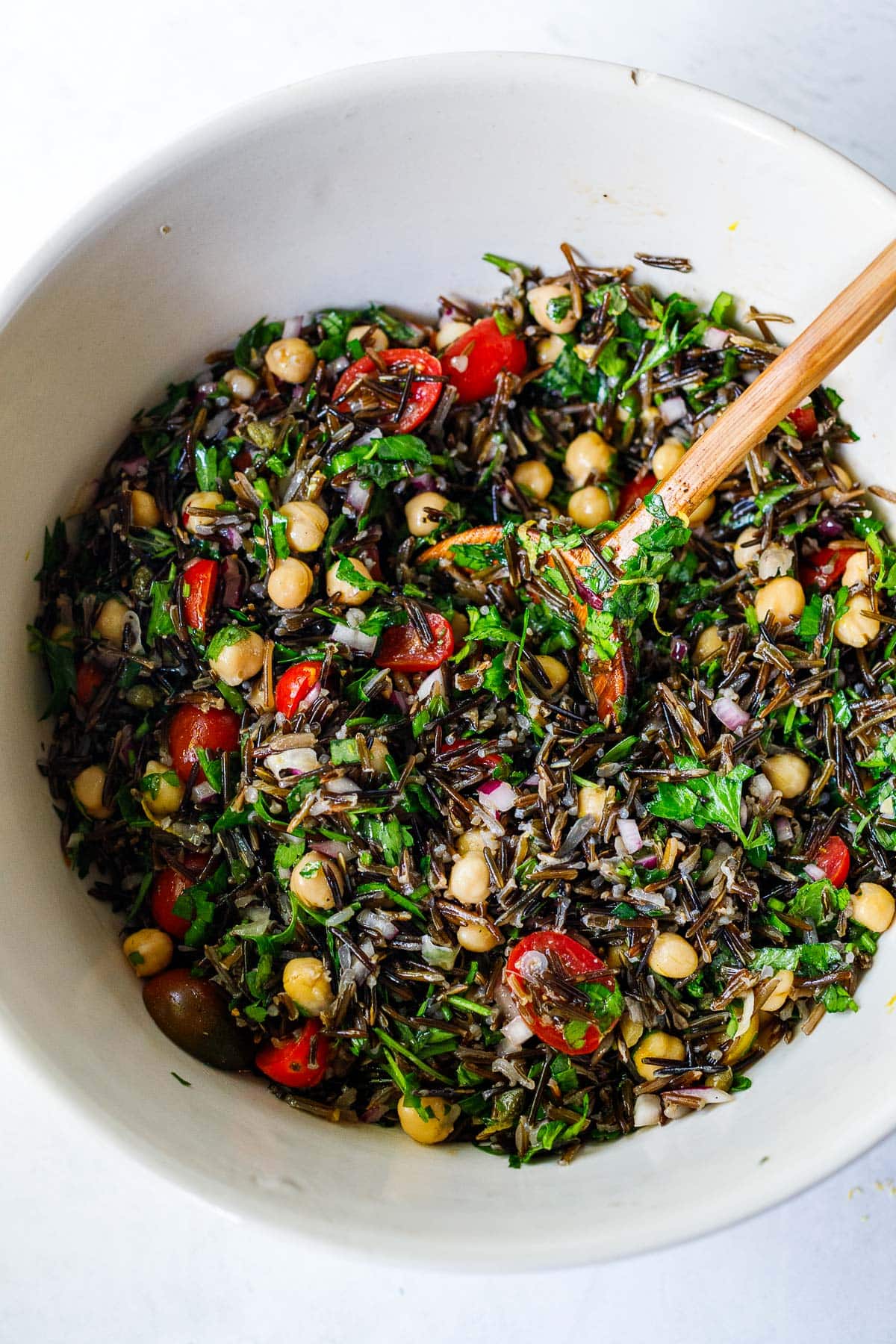 wood spoon mixing a wild rice salad in large white bowl