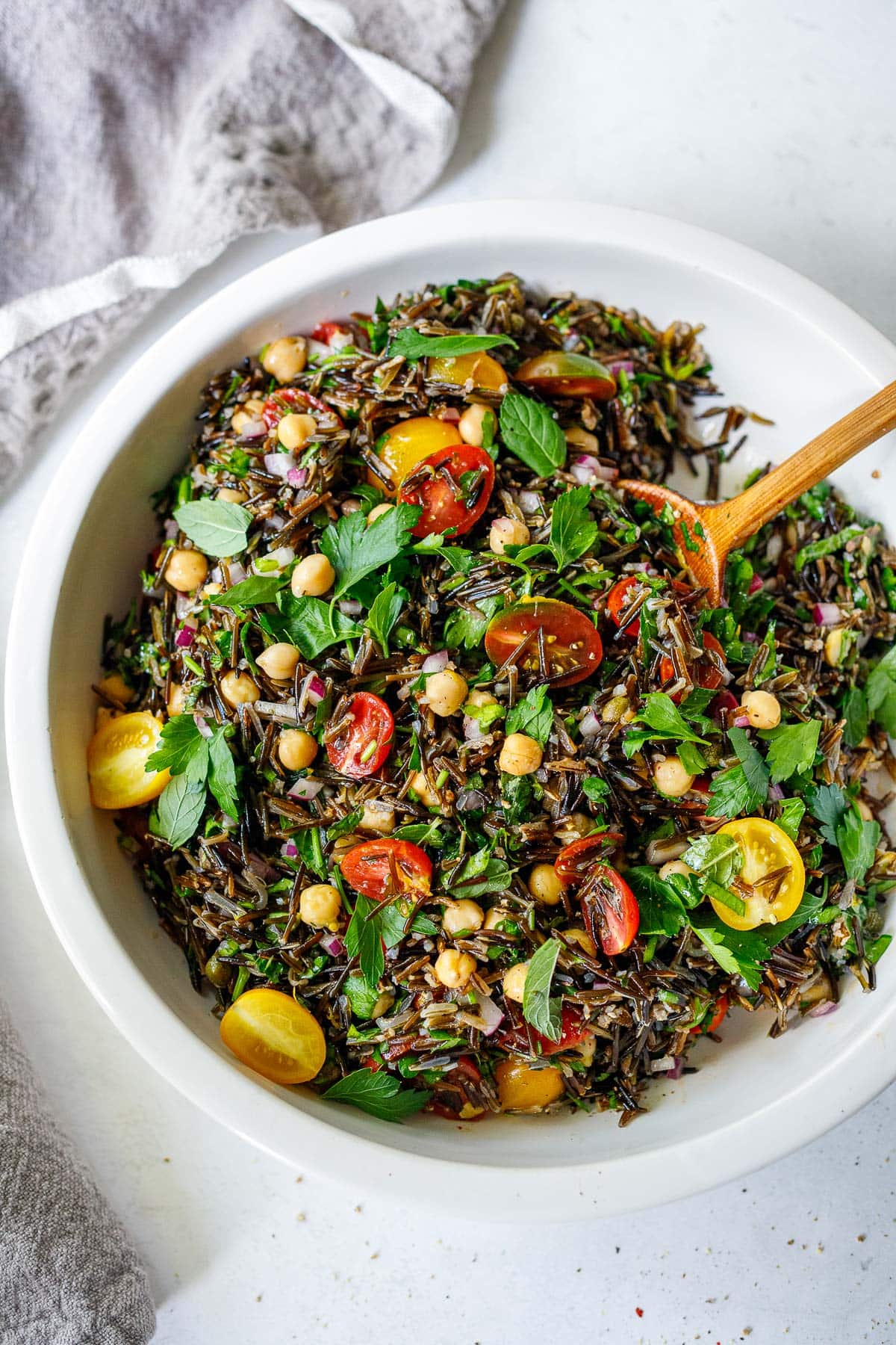 Wild rice salad with tomatoes and herbs in serving bowl with wood spoon.