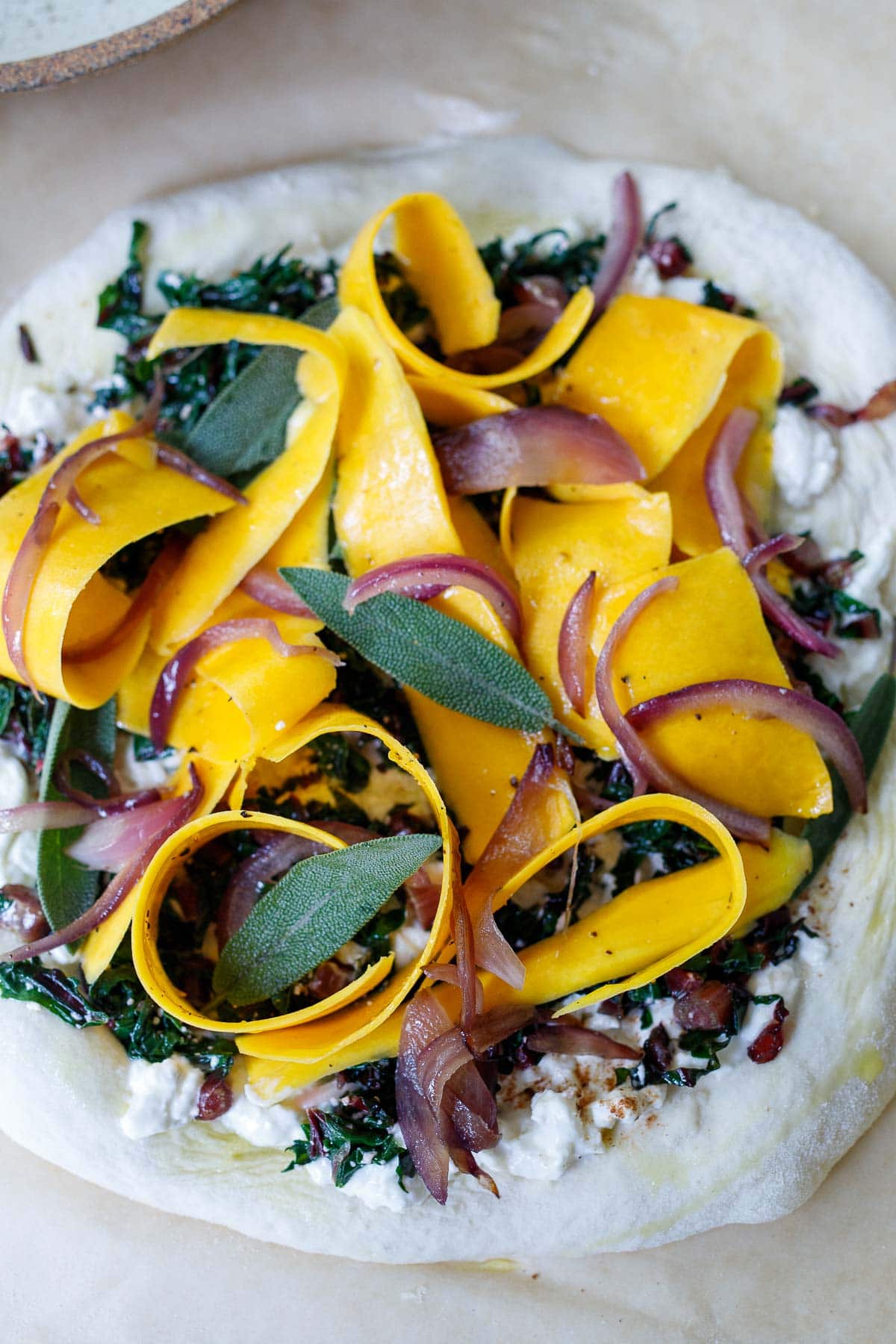 uncooked pizza with butternut squash, caramelized onion, sage