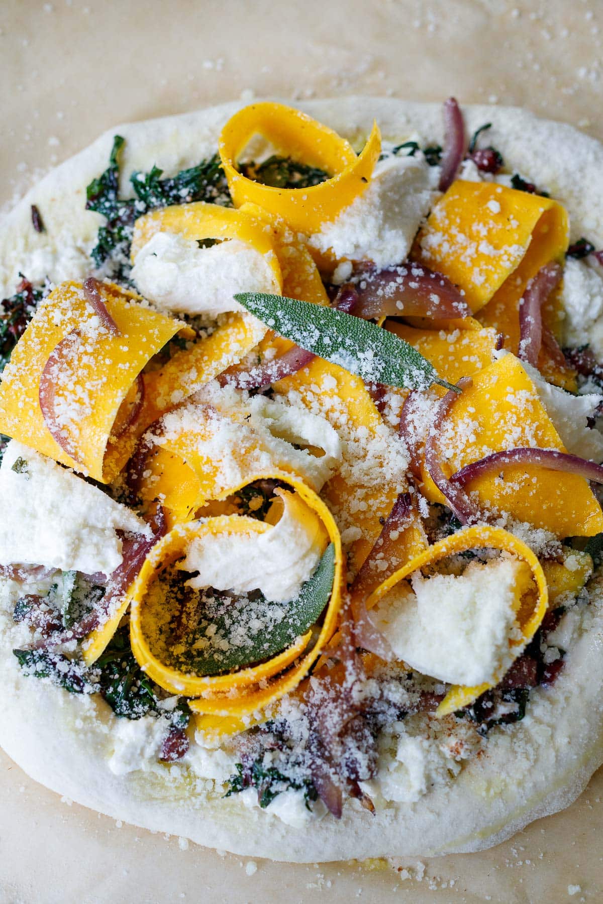 uncooked butternut squash pizza with pecorino cheese grated on top