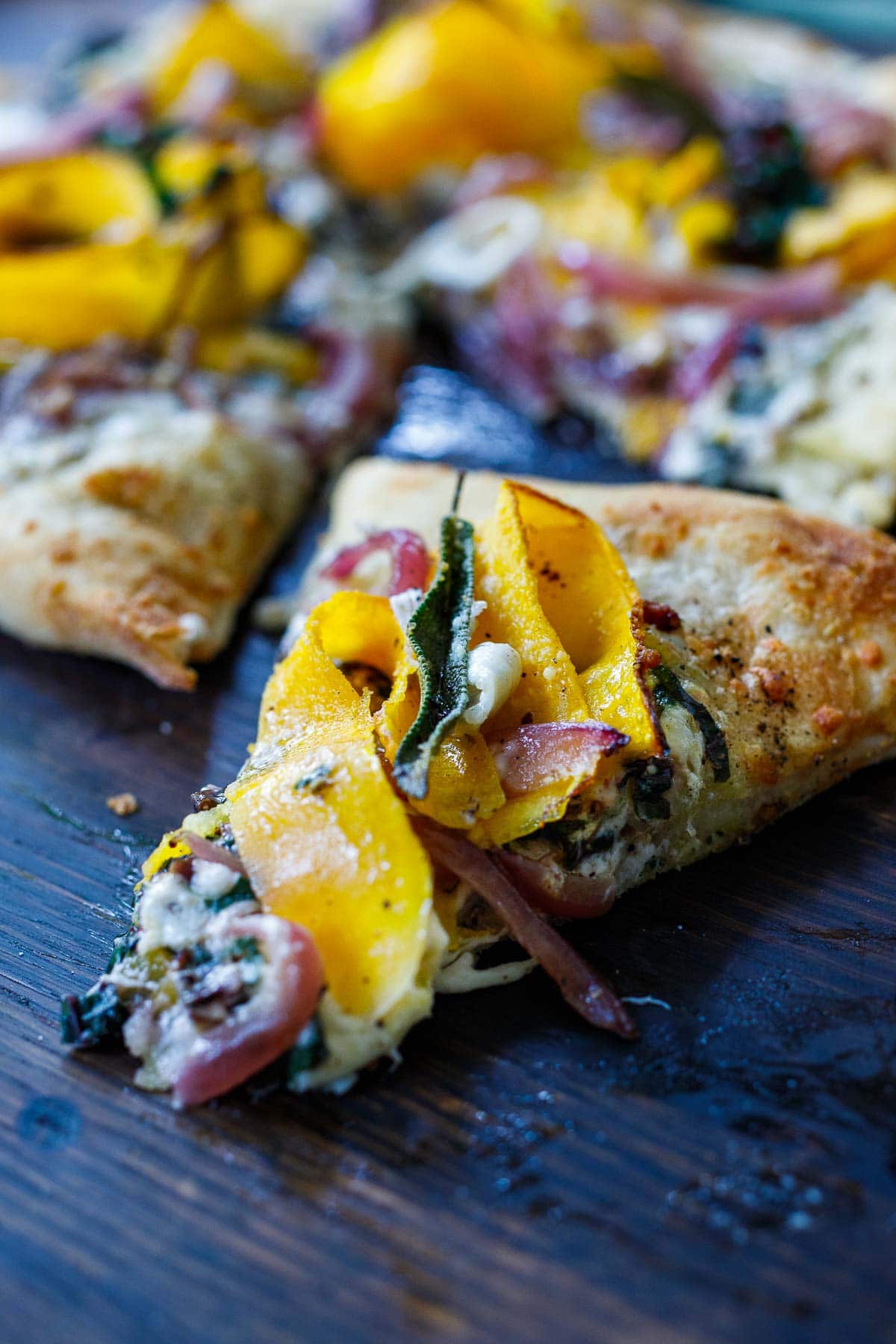 slice of butternut squash pizza topped with melted cheese, onion, sage