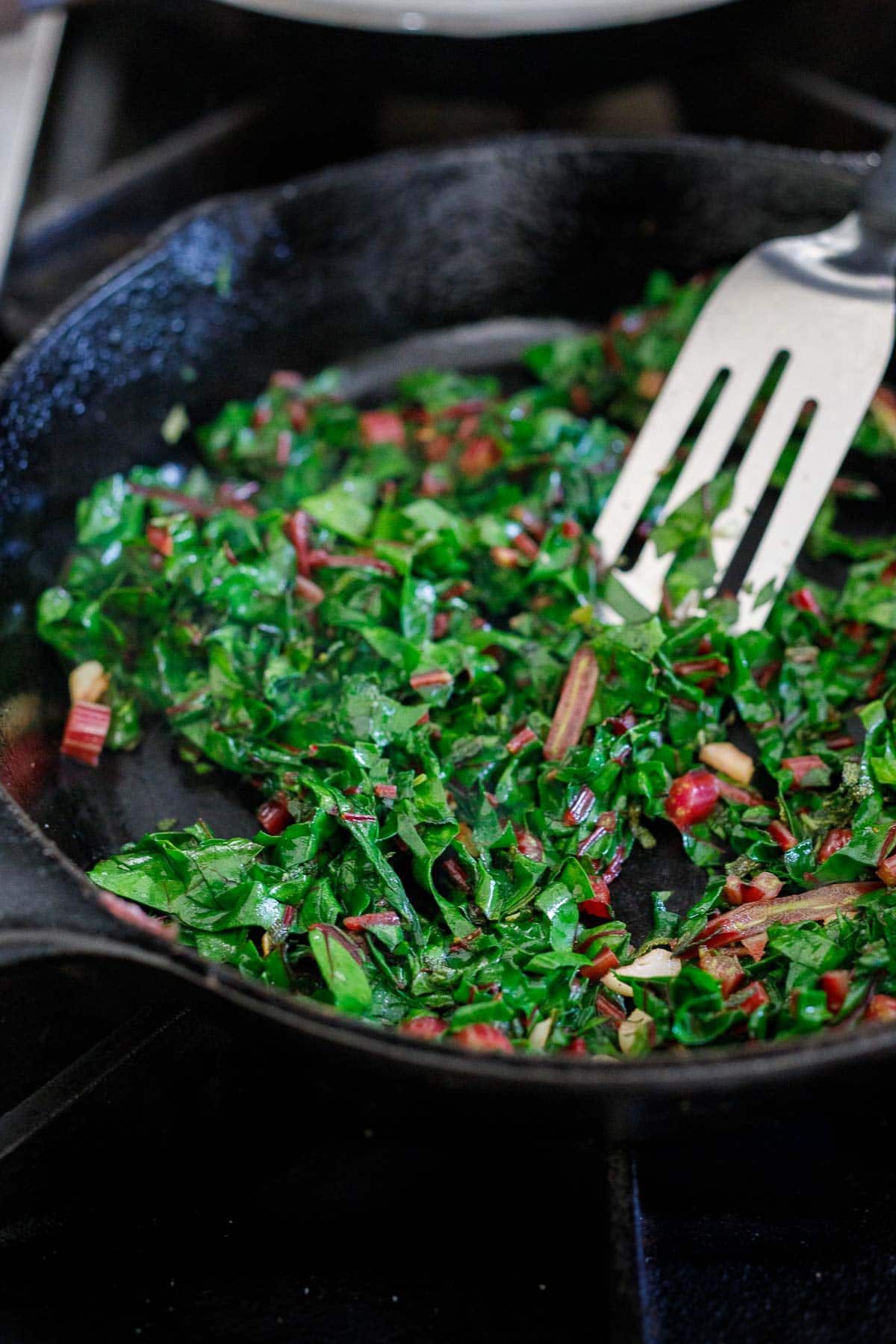 swiss chard cooking in cast iron skillet with spatula