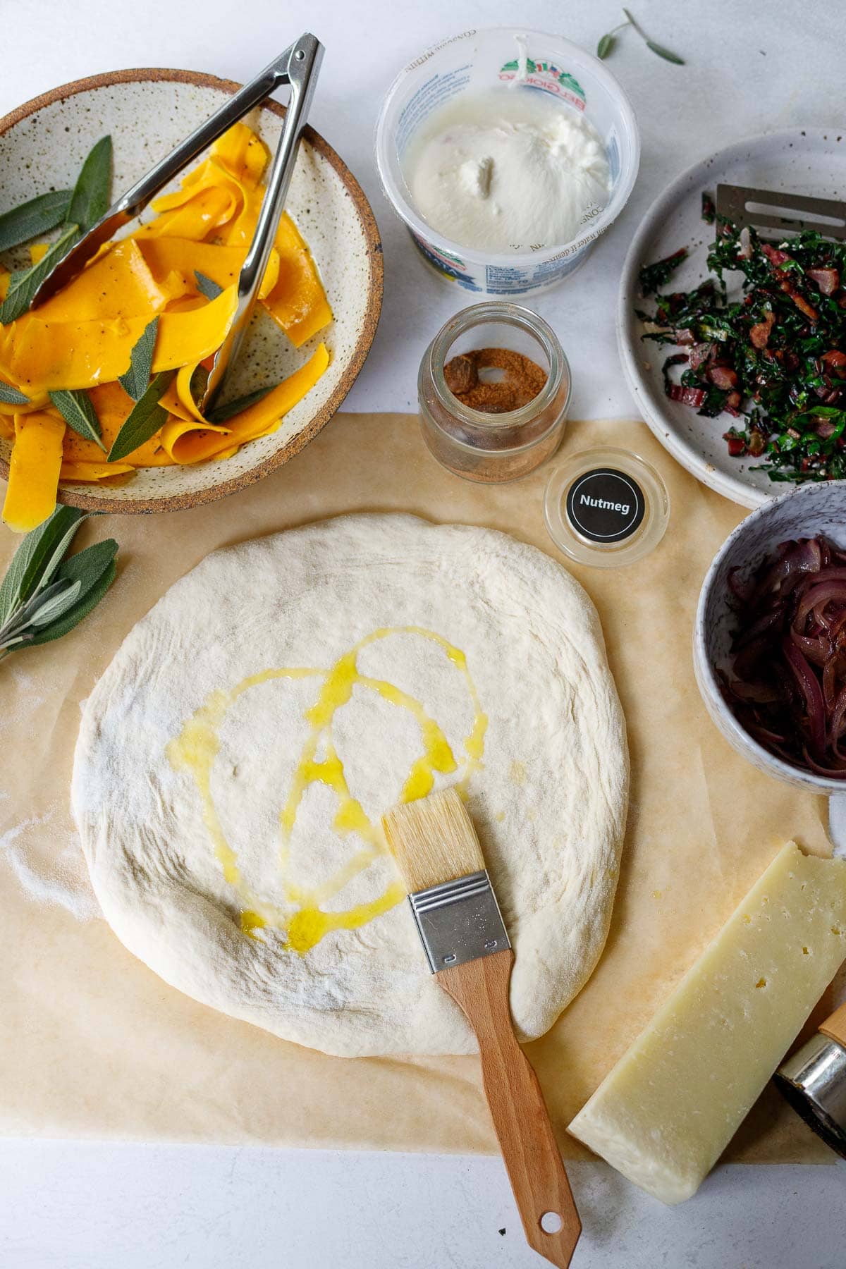 olive oil brush on rolled out dough surrounded by butternut squash pizza toppings