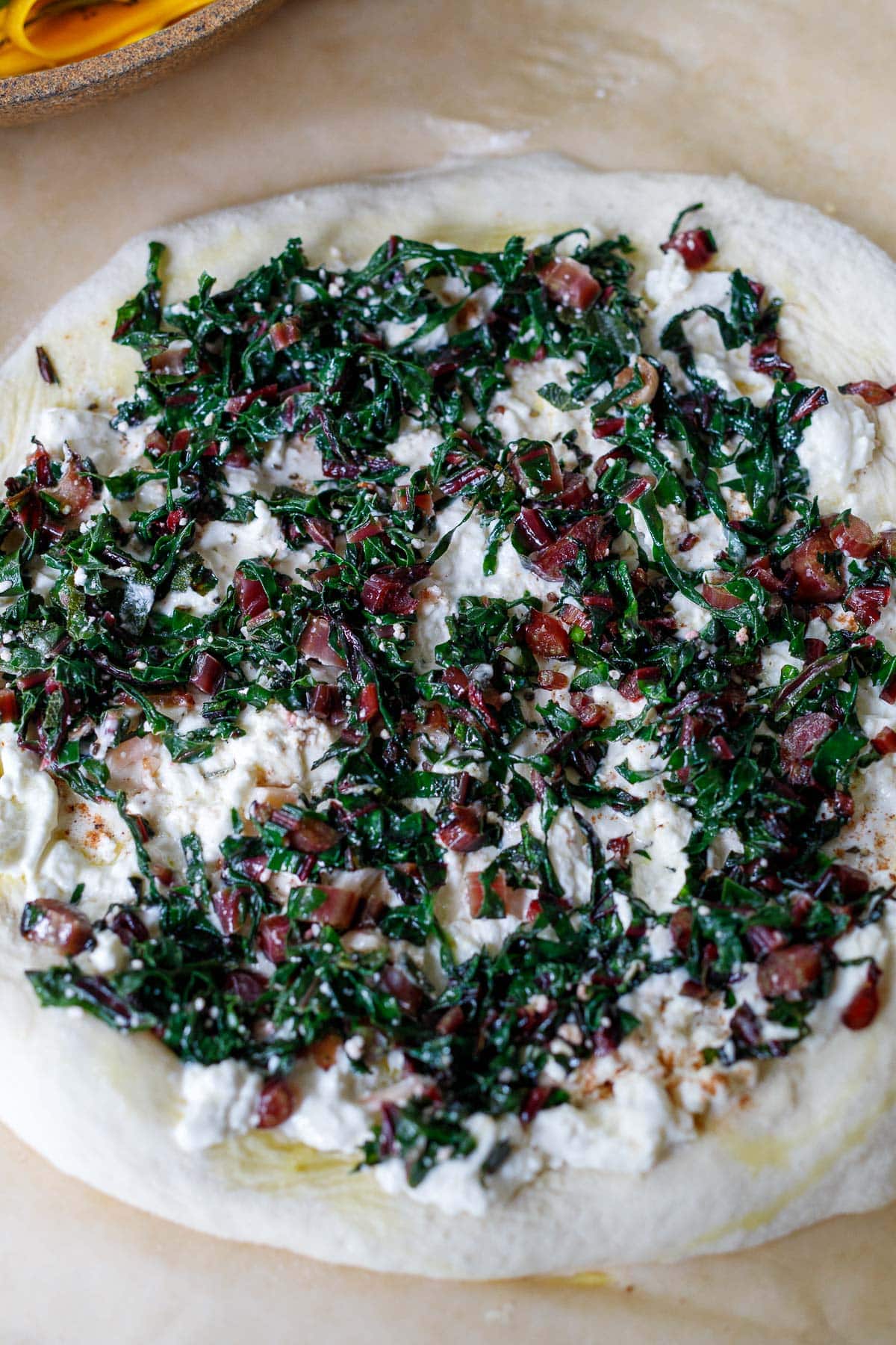 pizza dough rolled out with burrata cheese and wilted swiss chard on top