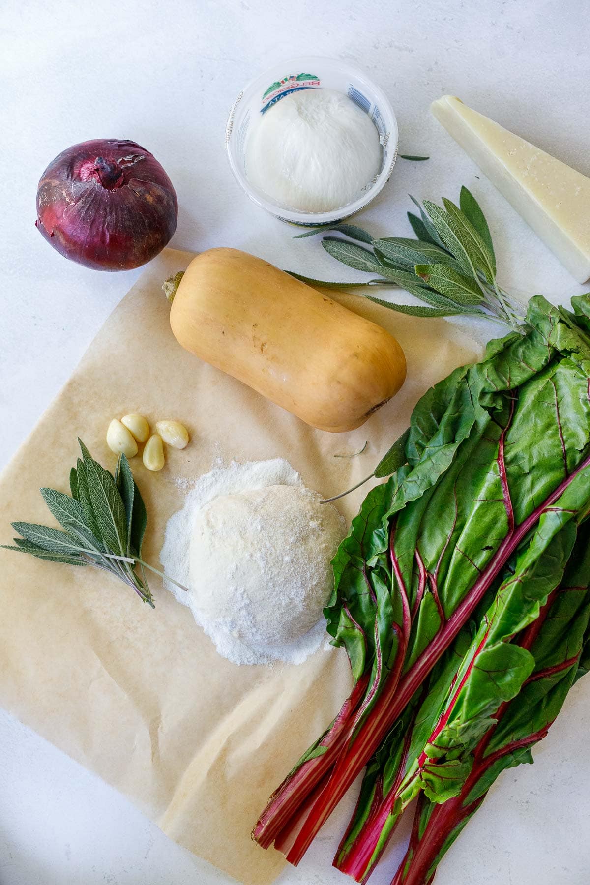 ingredients for butternut squash pizza laid out, dough, chard, sage, garlic, squash, onion, cheese