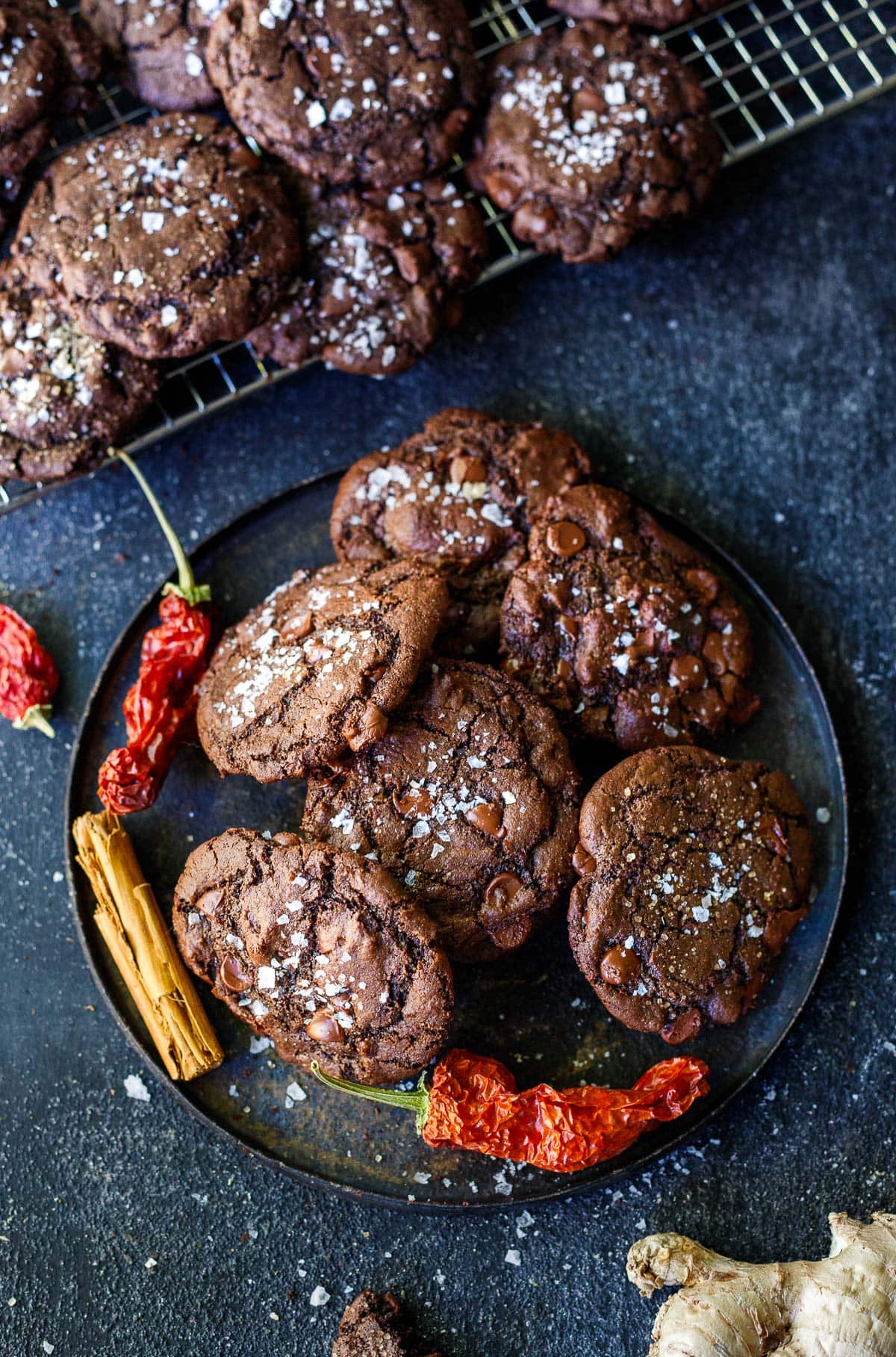 plate full of double chocolate chip cookies with flaky salt, cayenne pepper and cinnamon stick