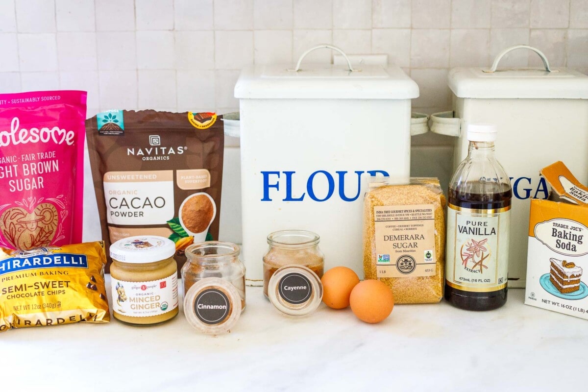 baking ingredients lined up on counter for making double chocolate chip cookies, flour, sugar, vanilla, eggs, cacao powder, spices