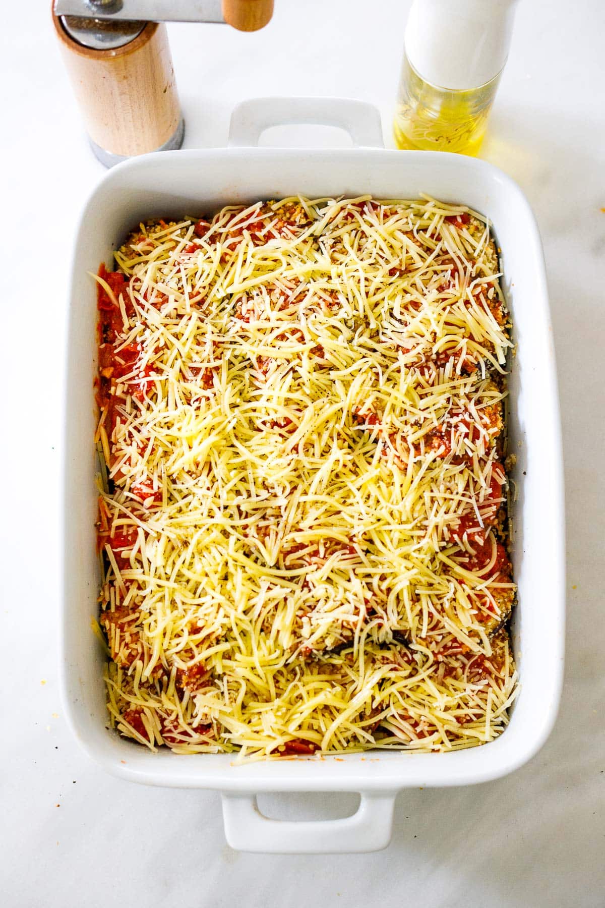 white baking dish with shredded mozzarella cheese on top of marinara sauce and eggplant slices