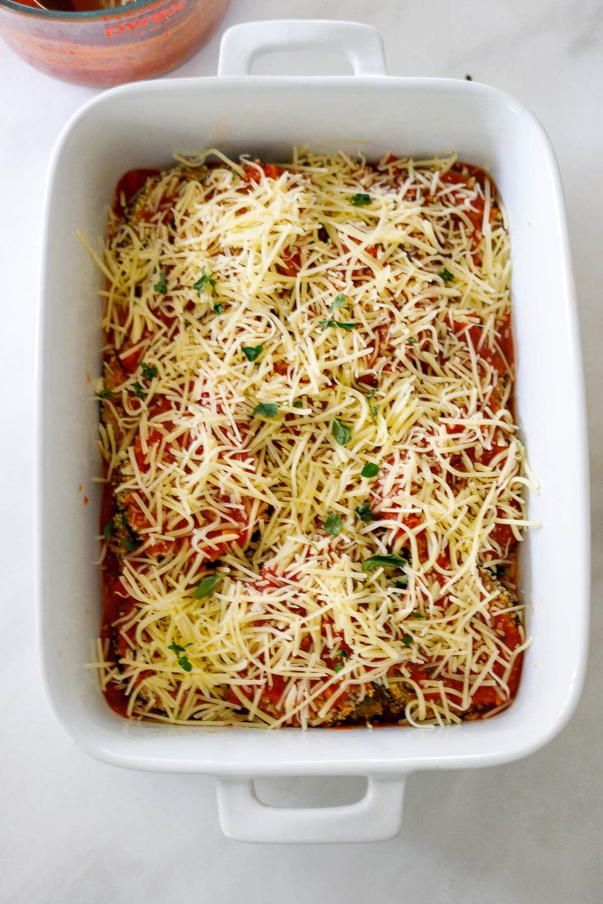 layer of shredded mozzarella over marinara sauce and eggplant underneath in white casserole dish