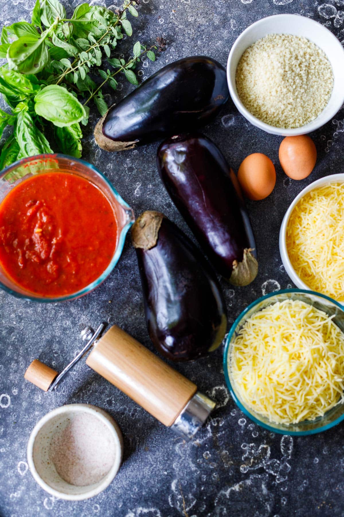 ingredients in eggplant parmesan laid out; eggplant, cheese, eggs, marinara sauce, basil.