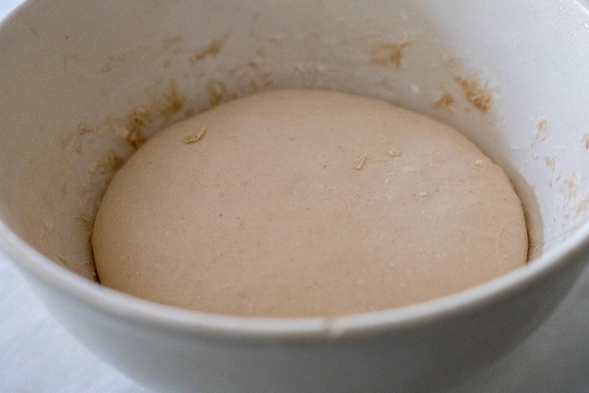 perfectly proofed dough in a white bowl after rising overnight. 