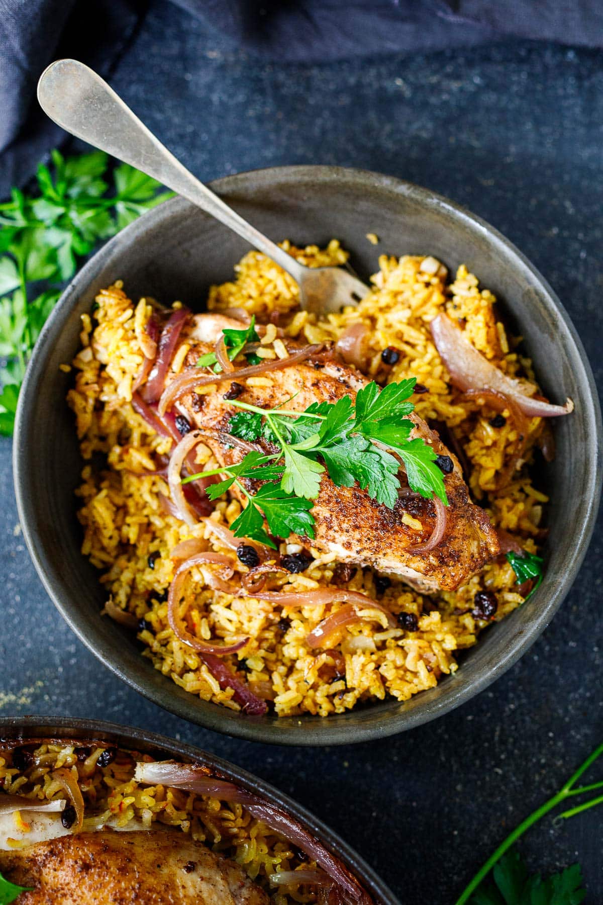 bowl of Persian chicken on bed of saffron rice with caramelized onions and barberries, garnished with parsley