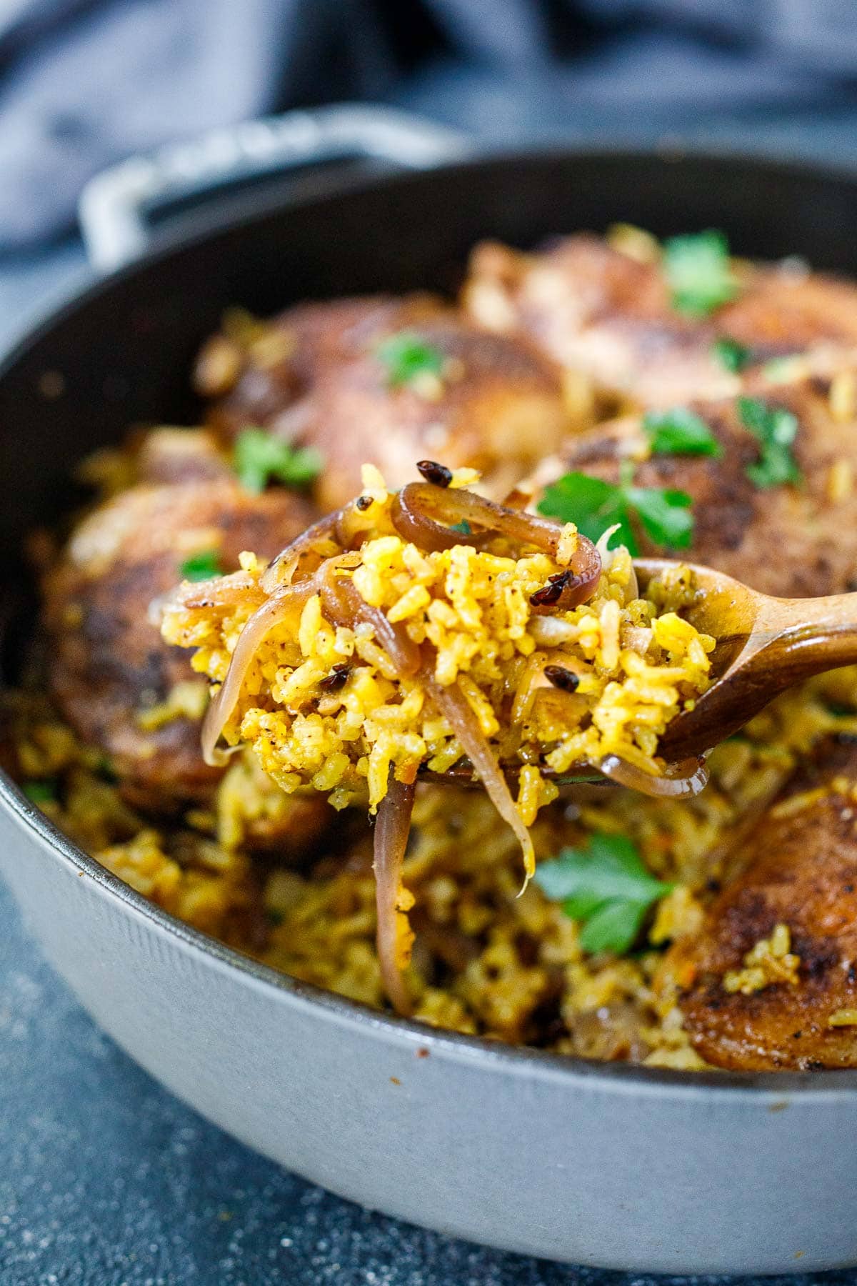 wood spoonful of saffron rice with caramelized red onions and barberries being lifted from dutch oven with Persian chicken