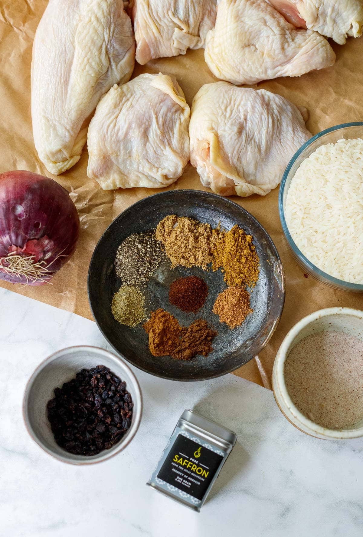 ingredients for persian chicken on parchment paper - chicken, rice, spices, onion, salt, barberries