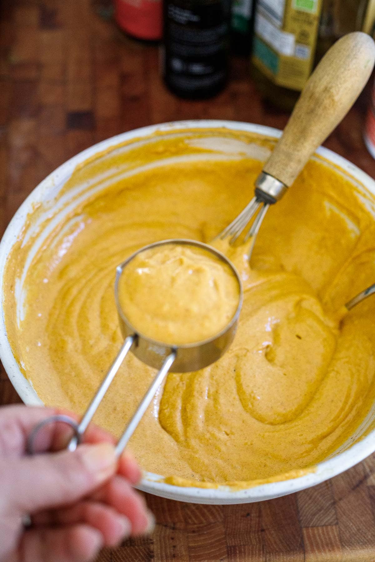 measuring cup filled with batter held over top of bowl with pumpkin pancake batter