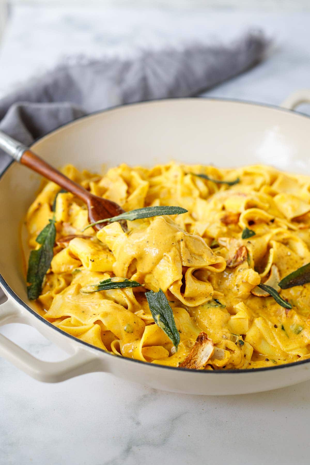 creamy papperadelle pumpkin pasta with crispy sage leaves and garlic chips being lifted from pot with a wood fork