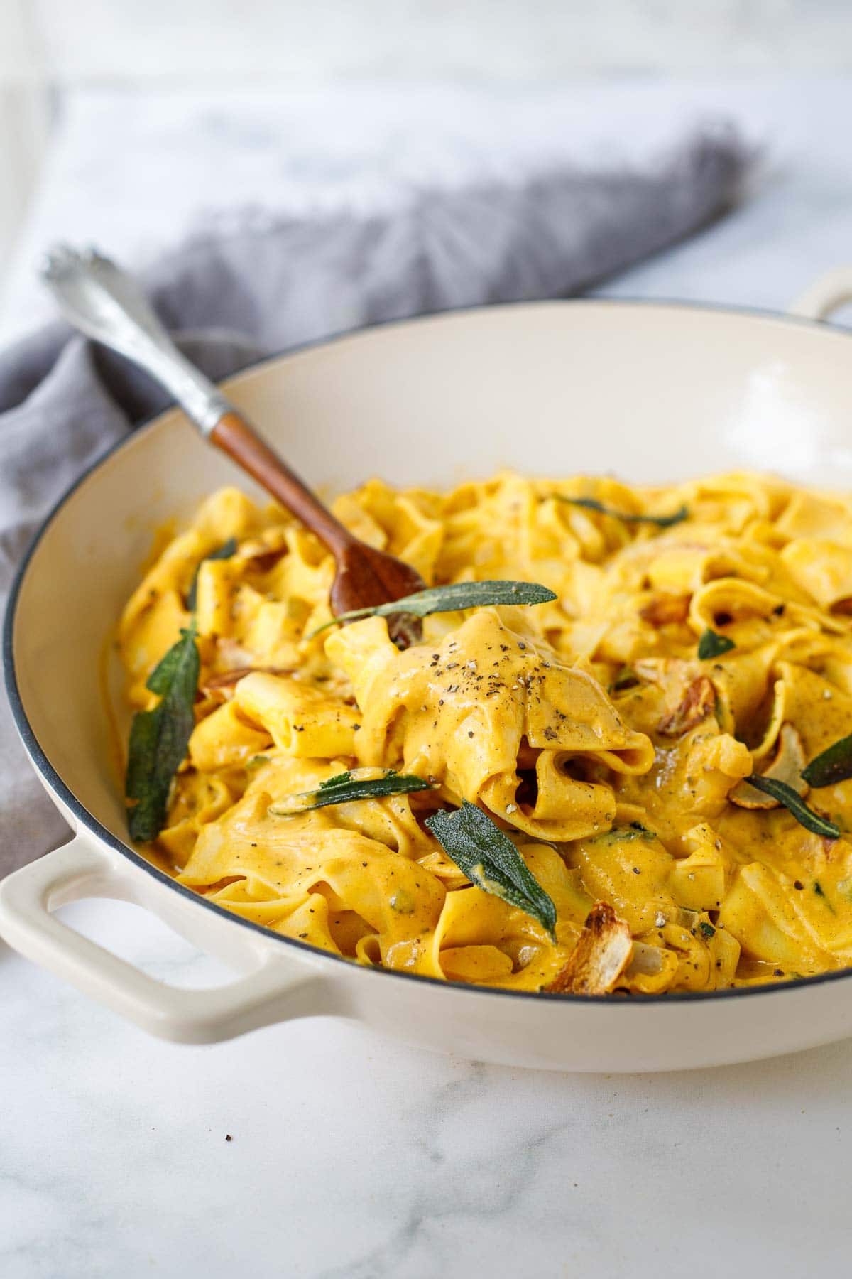 spoonful of saucy pumpkin pasta being lifted from pasta with sage and garlic chip garnish and black pepper