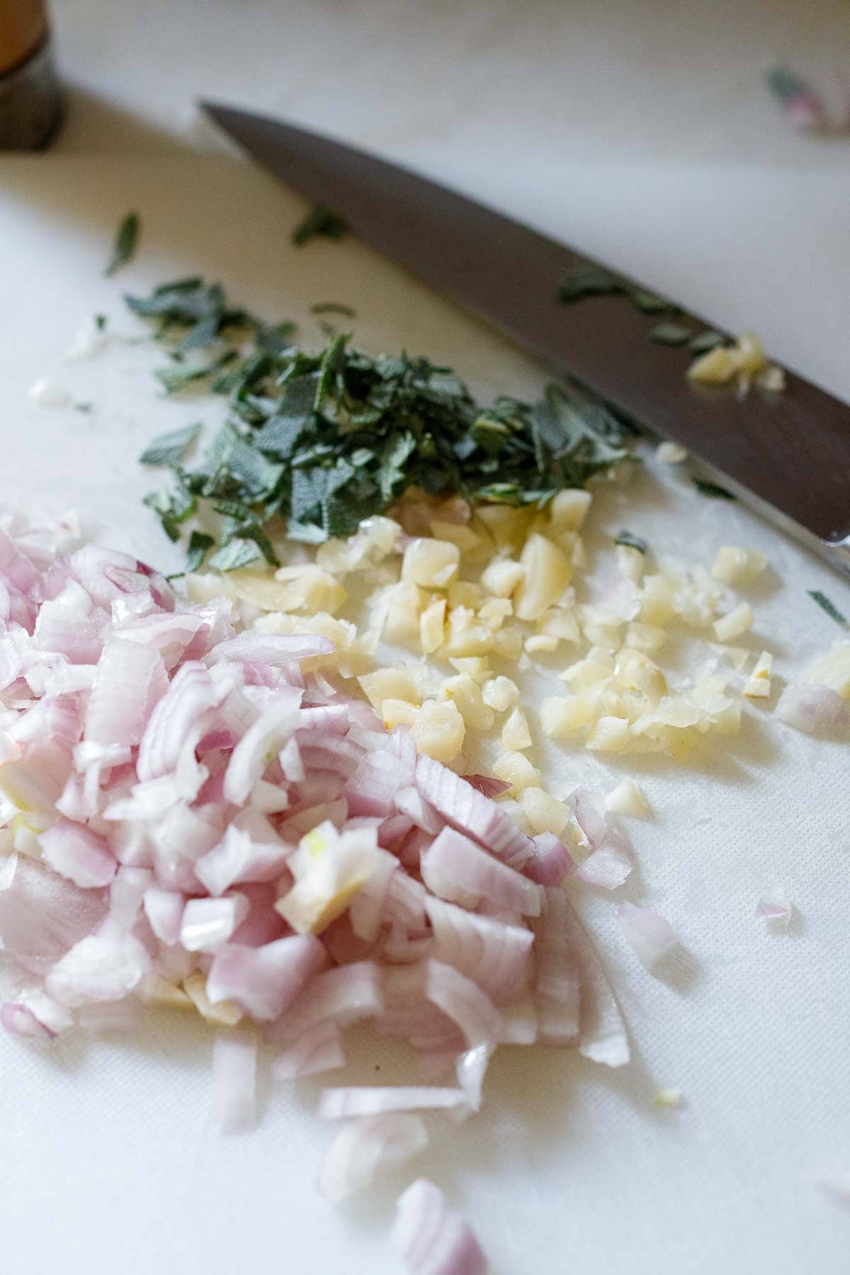 chopped shallot, garlic, and sage on cutting board with knife