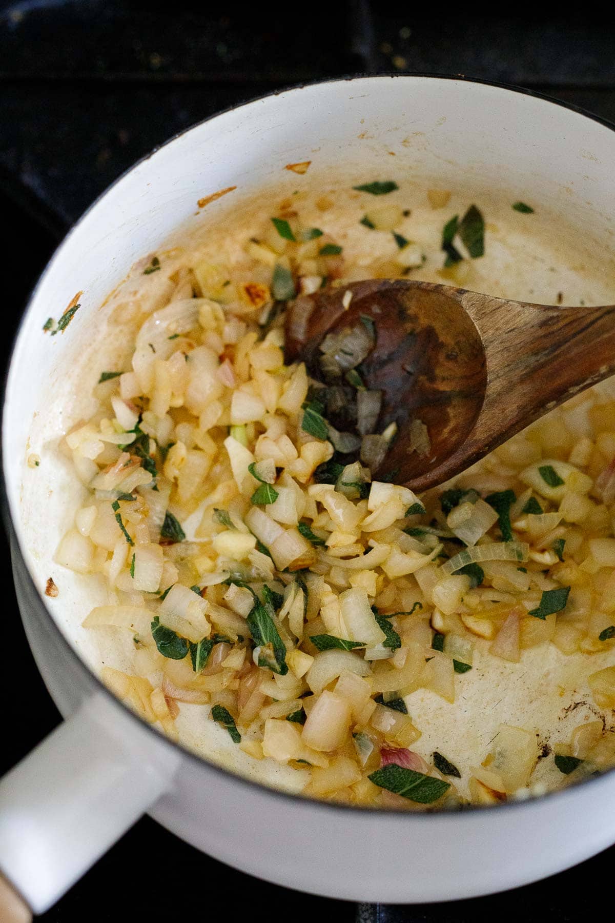 pot with sauteed garlic, shallot, and sage stirred by wood spoon