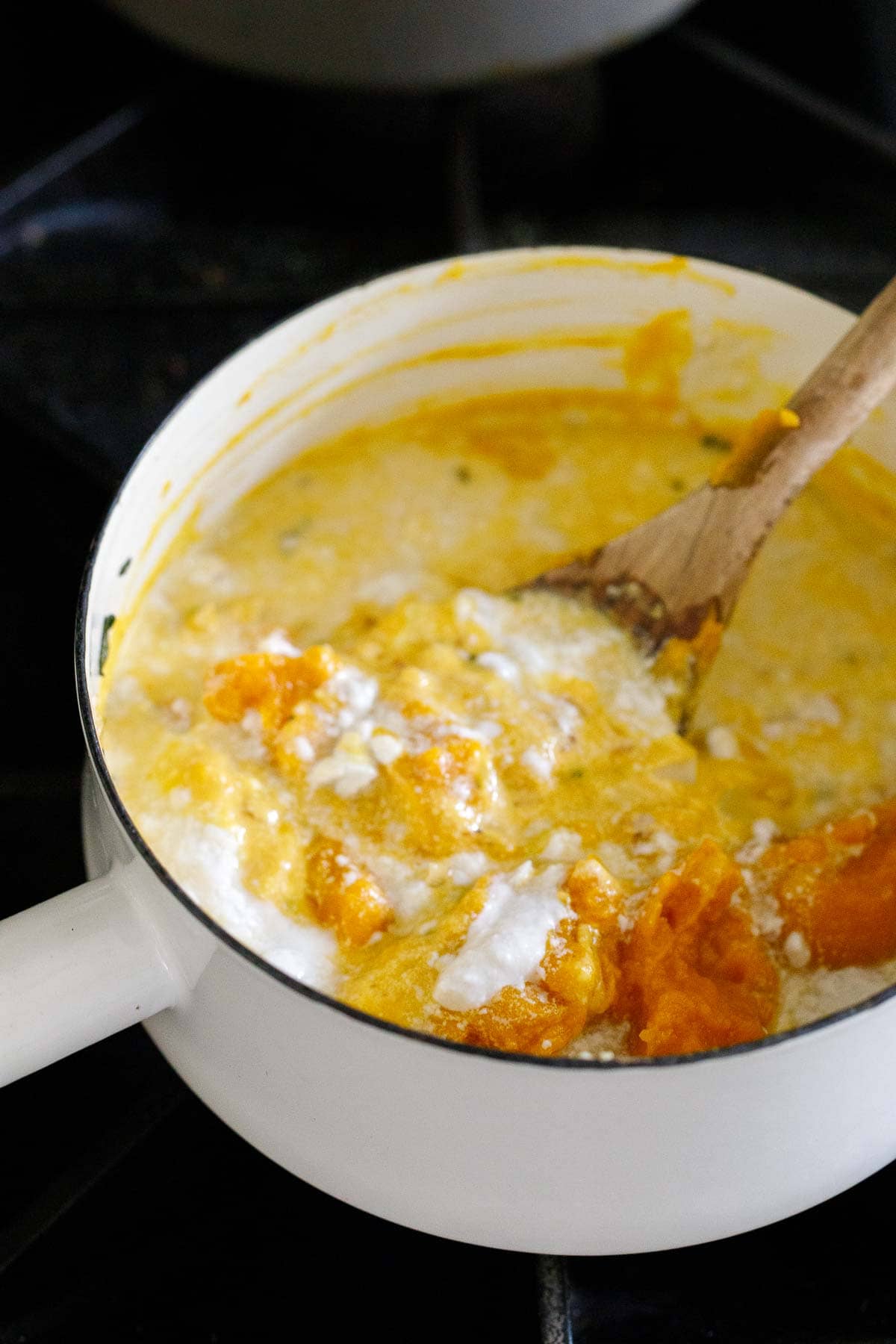 sauce in a pot with pumpkin puree and coconut cream being stirred by wood spoon