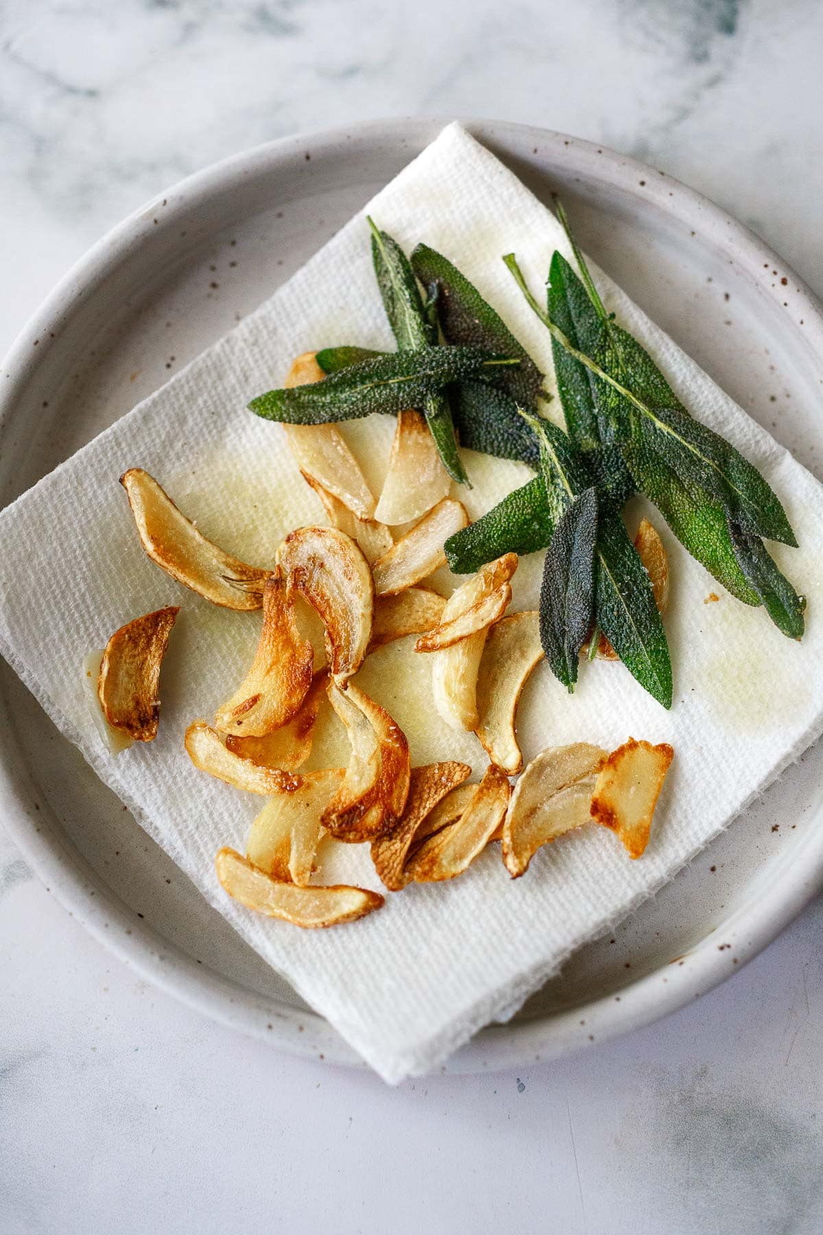 garlic chips and crispy sage laid out on folded paper towel on ceramic plate