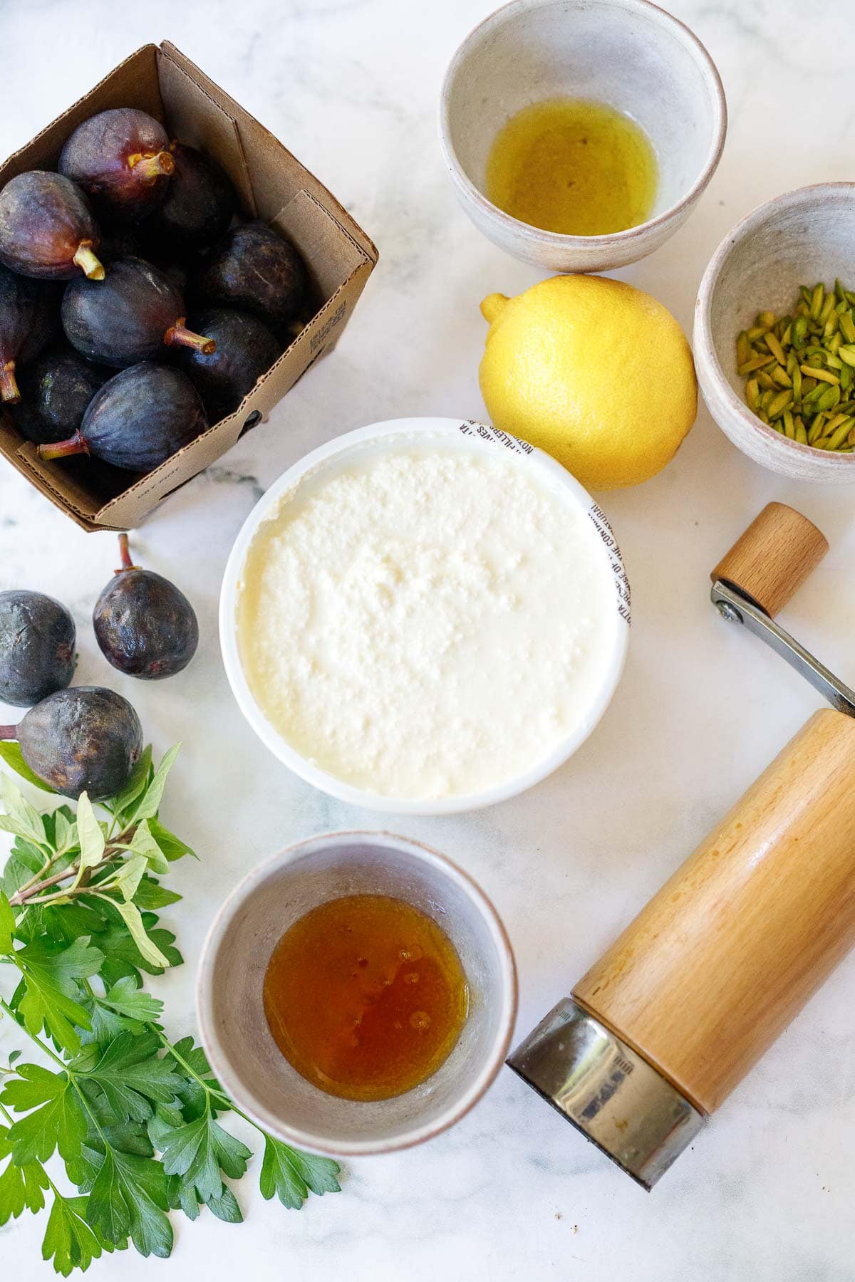 ingredients for whipped ricotta on table, ricotta cheese, lemon, honey, pistachios, figs, herbs