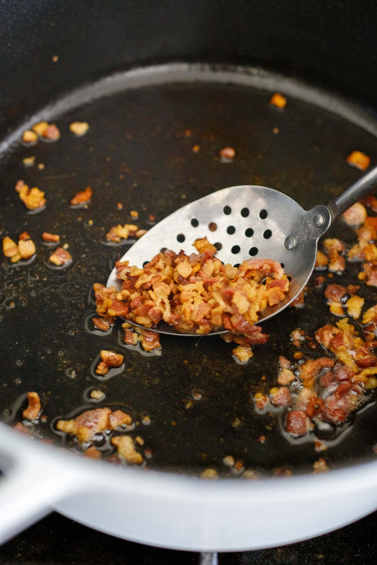 cooked crispy bacon bits in pot with slotted spoon