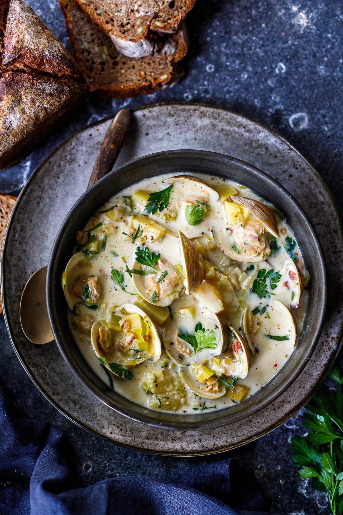 bowl of clam chowder with shells, fresh herbs, bacon bits, and potatoes